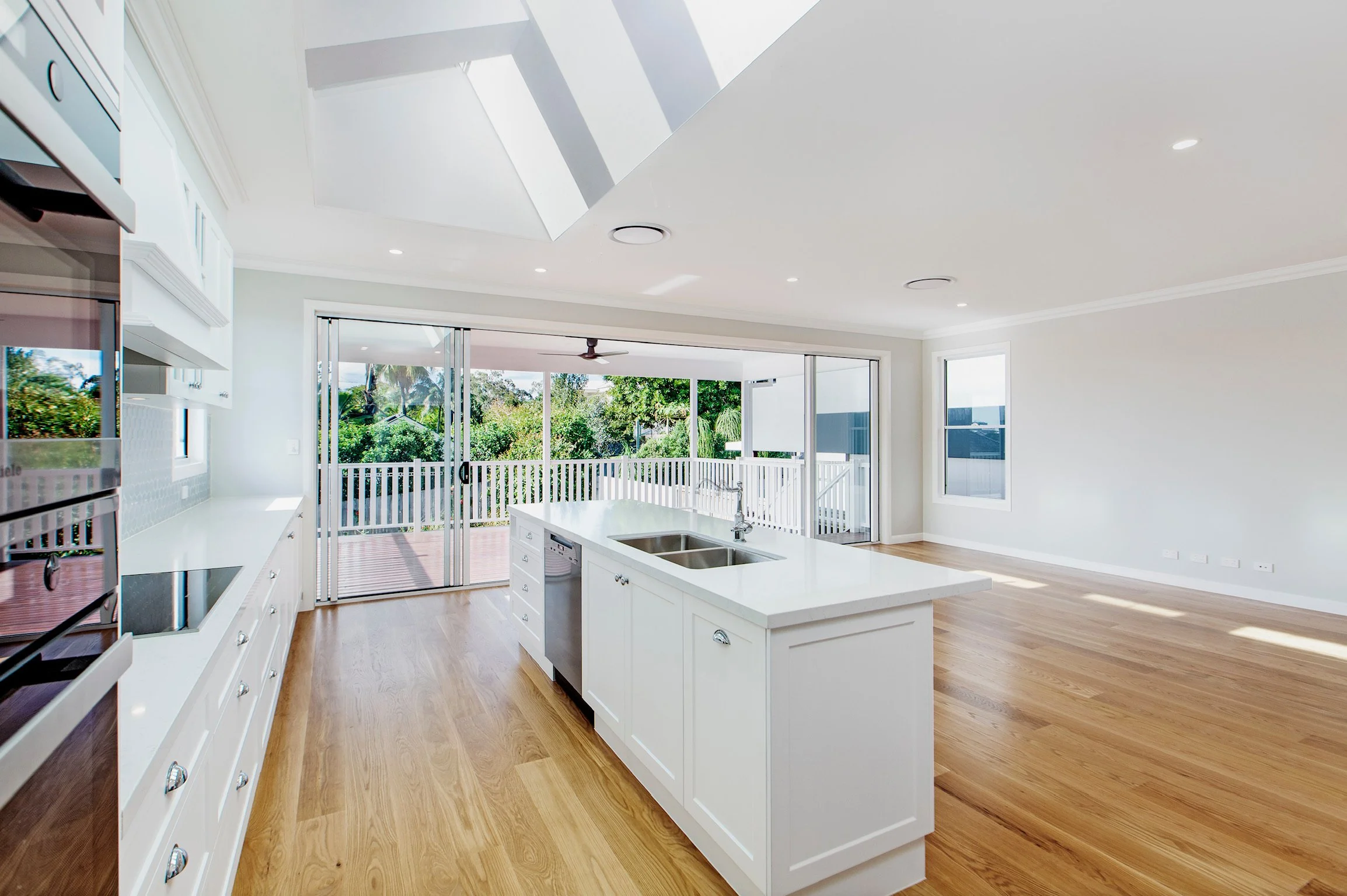 Bright and spacious white kitchen with a kitchen island, hardwood flooring, large sliding glass doors, and an outdoor view of trees and a porch.