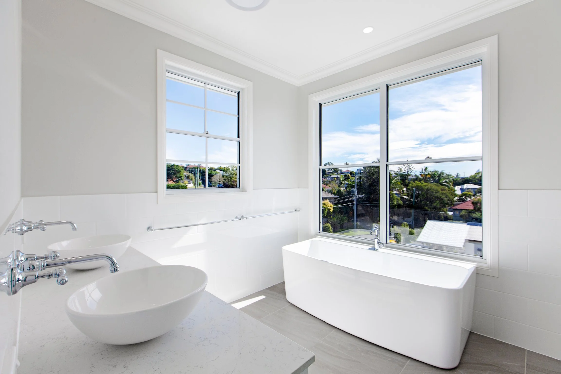 Modern bathroom with large windows, a bathtub, and a white sink with chrome fixtures.