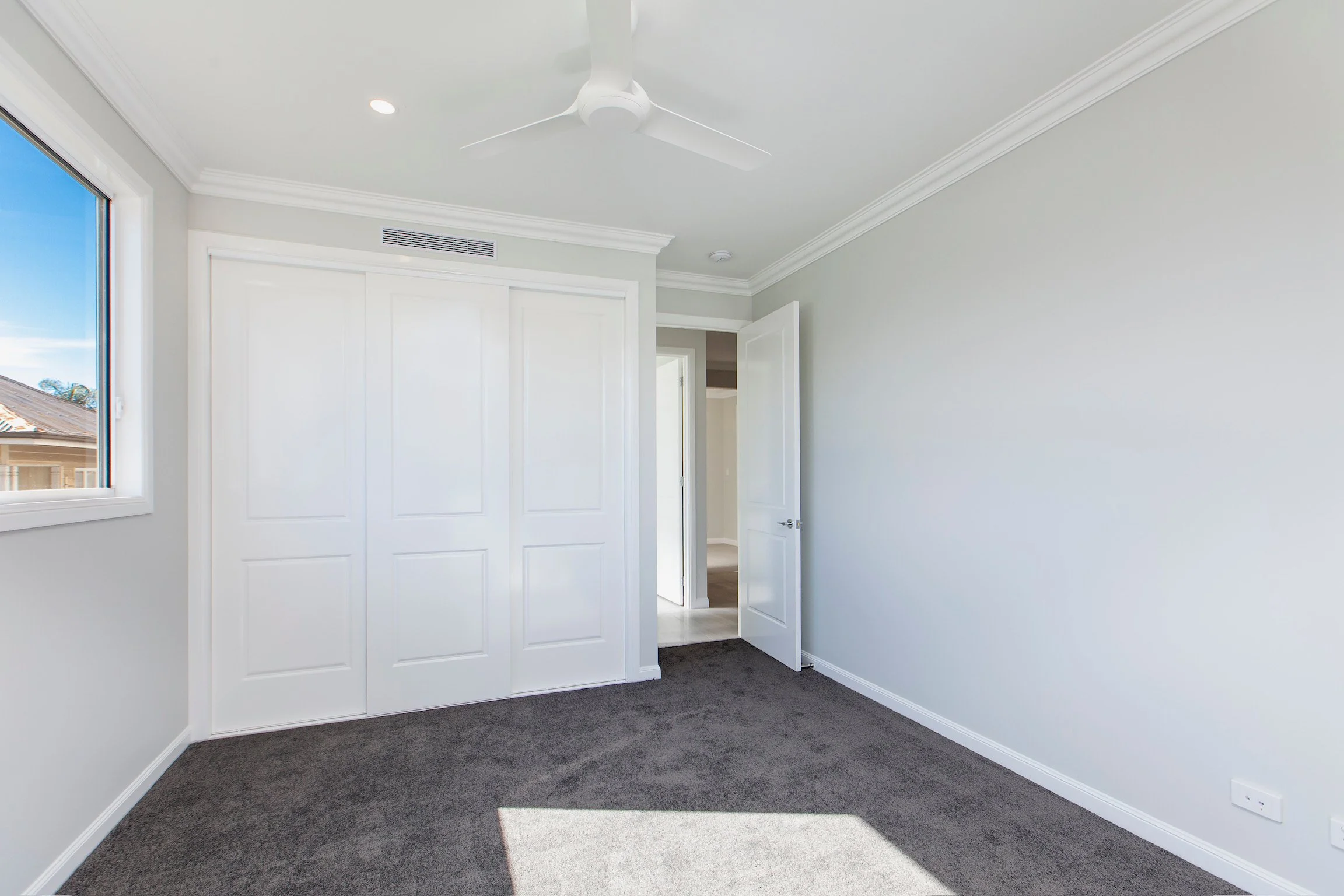 Empty room with gray carpet, white walls, a window showing a view outside, a ceiling fan, and a partially open closet door.
