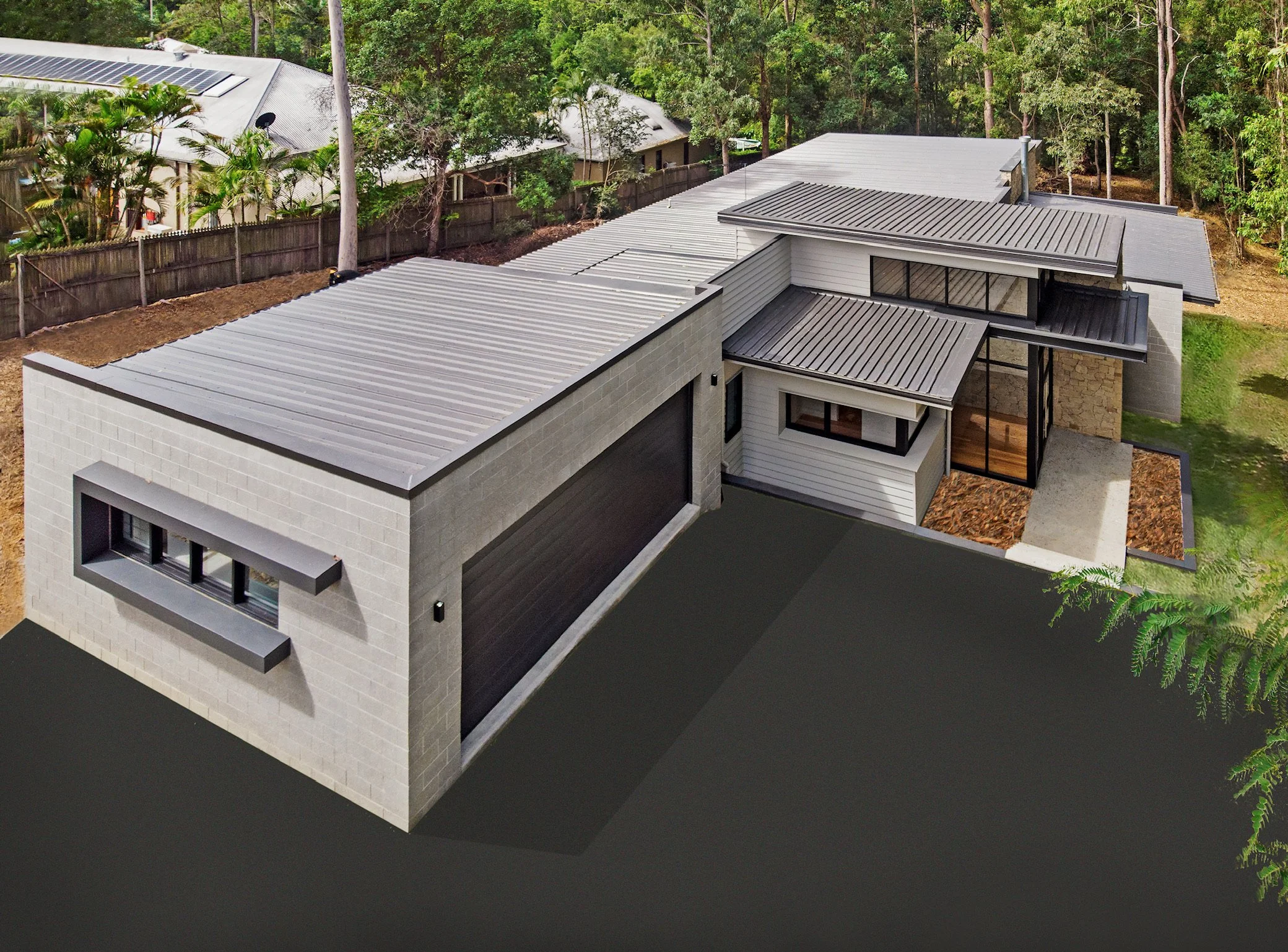 An aerial view of a modern house with metal roofs surrounded by trees and a fence.