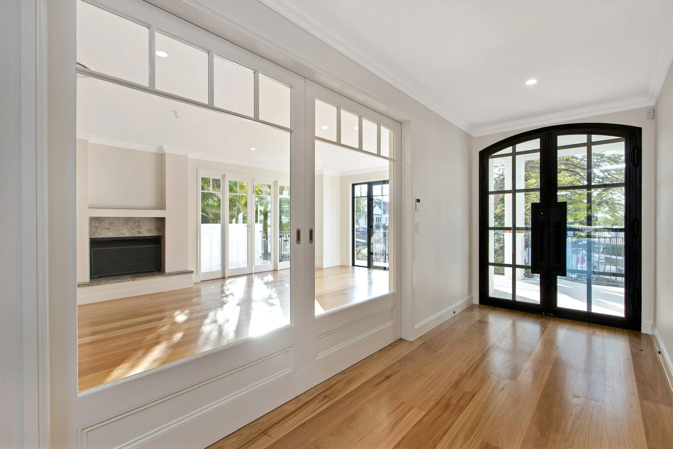 Interior view of a bright, modern living space with large windows and hardwood floors, seen through decorative glass panels.
