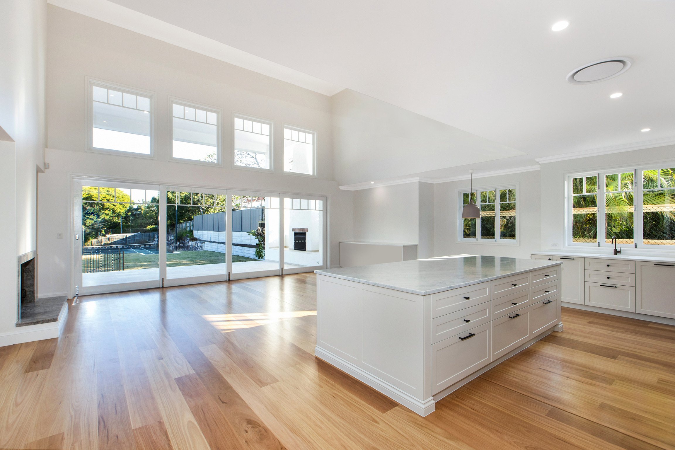 Spacious bright open-concept kitchen and living room with hardwood floors, white cabinetry, large windows, and a view of the backyard.