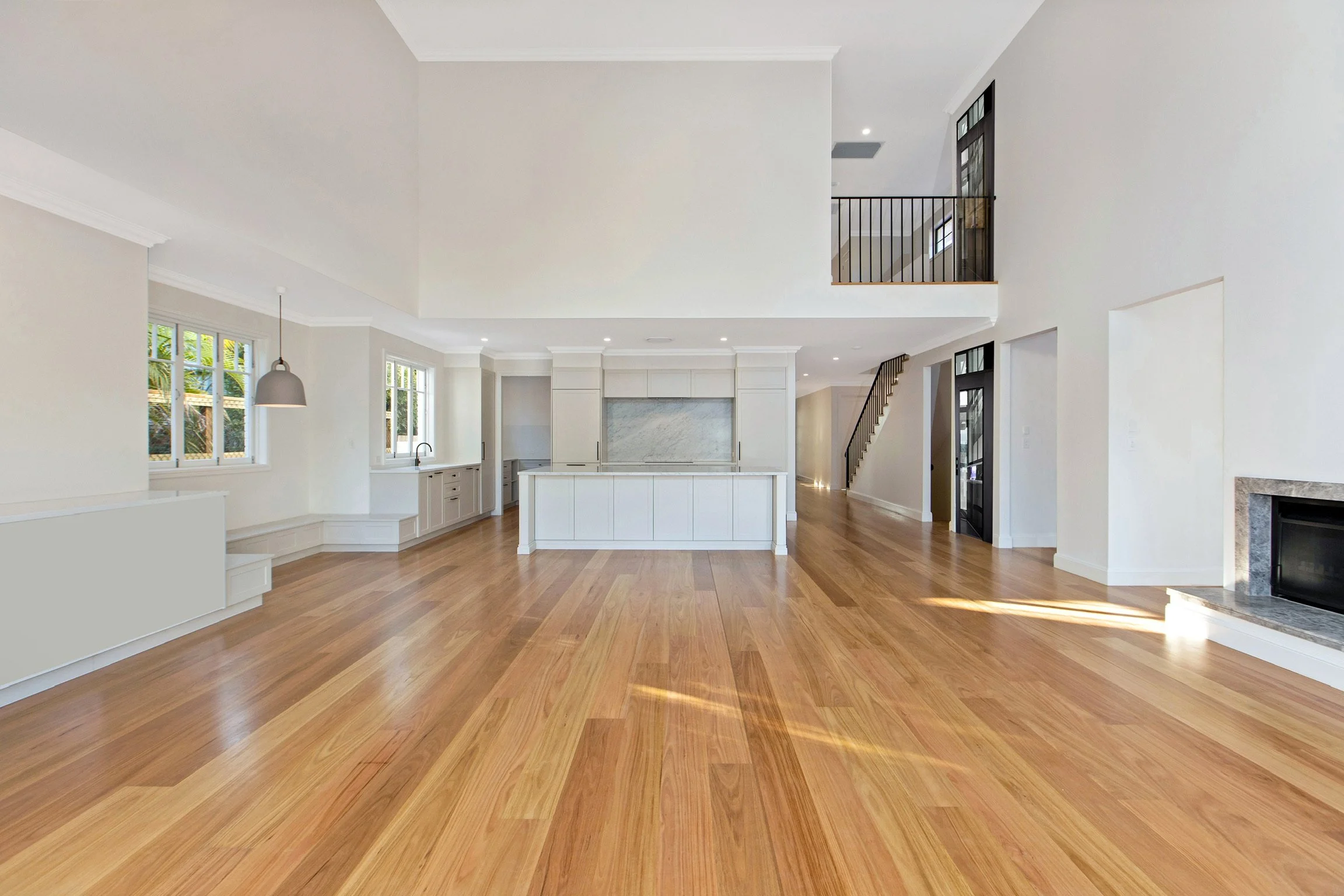 Open-concept living space with hardwood floors, white walls, large windows, a fireplace, and a kitchen with an island. Stairs lead to a loft area.