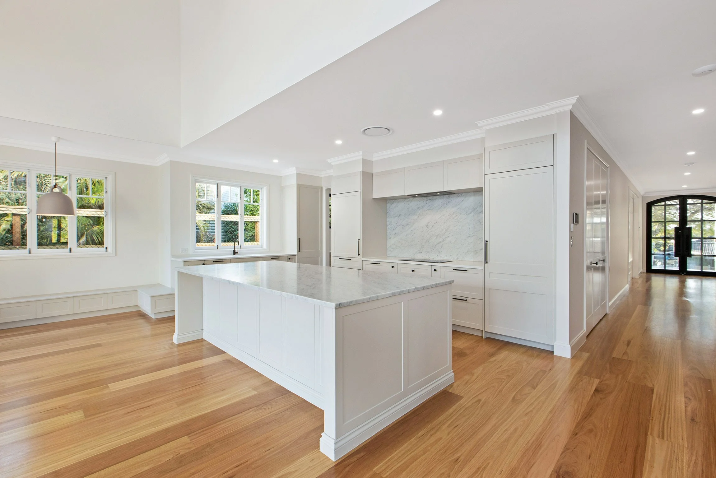 Bright modern kitchen with white cabinets, marble countertops, a large island, hardwood floors, and big windows.