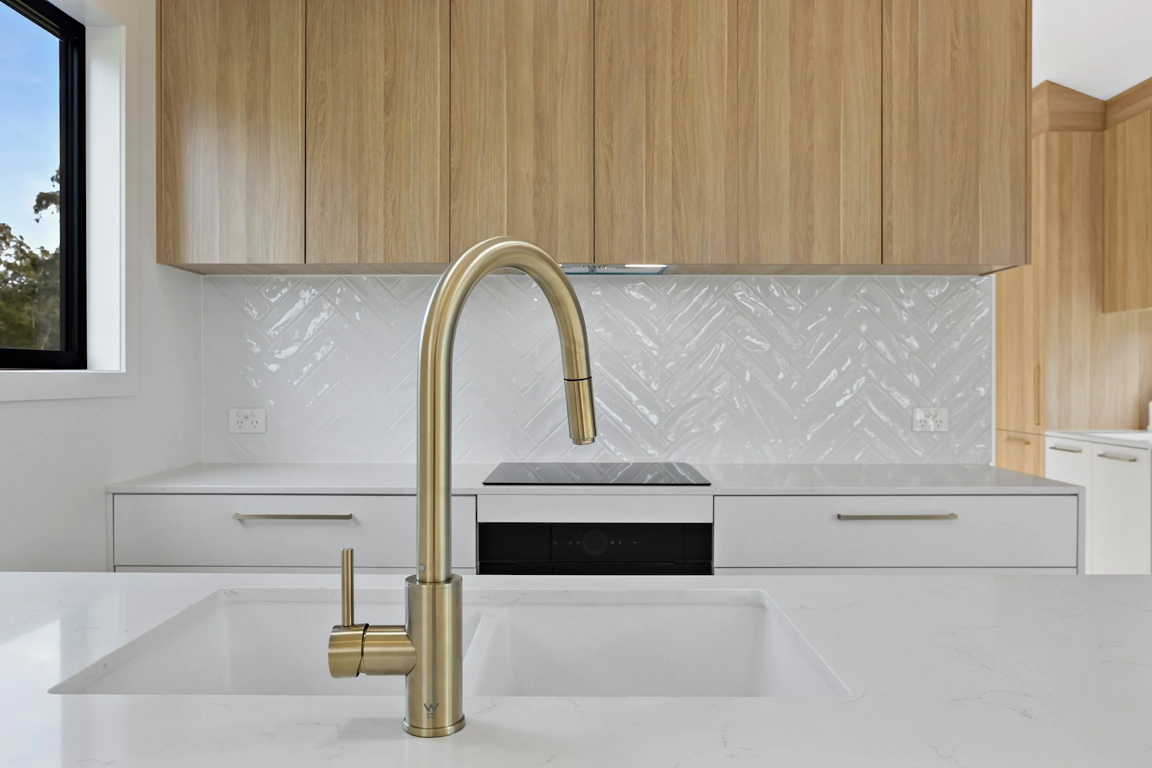 Modern kitchen with wooden upper cabinets, white tile backsplash, and a gold faucet over a white island countertop.