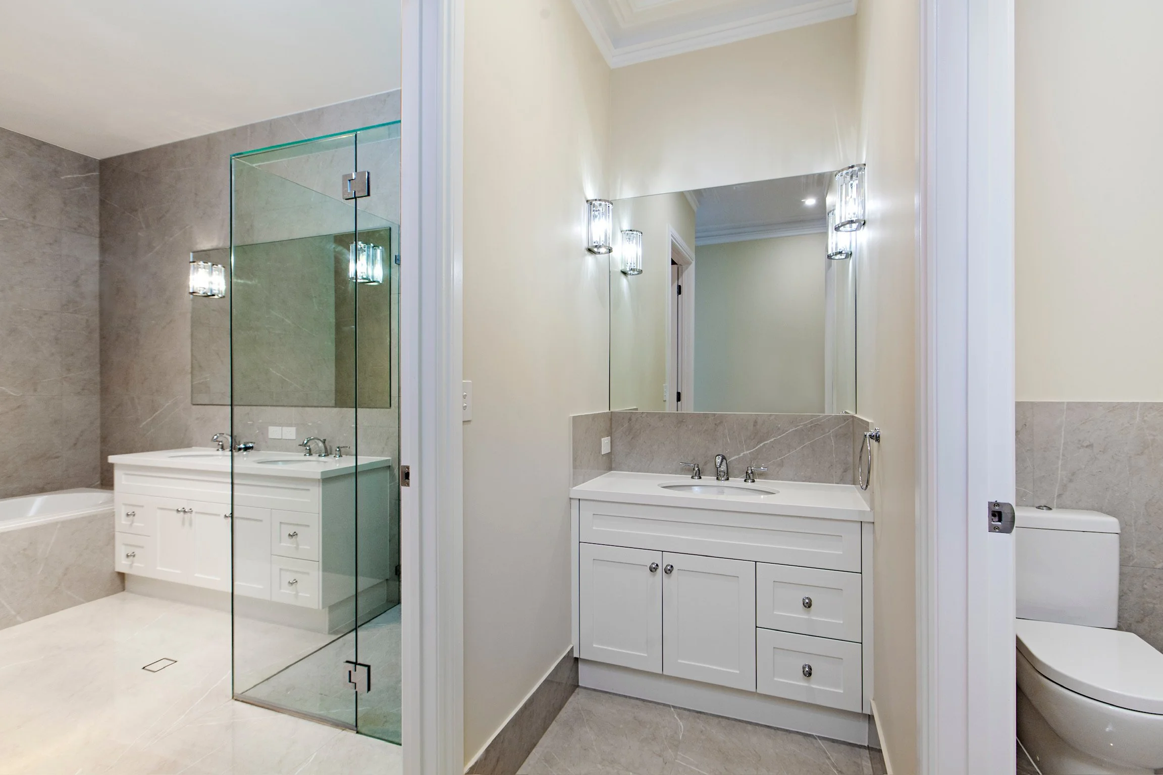 Modern bathroom with a large mirror, white vanity with two sinks, beige walls, and a glass-enclosed shower area.