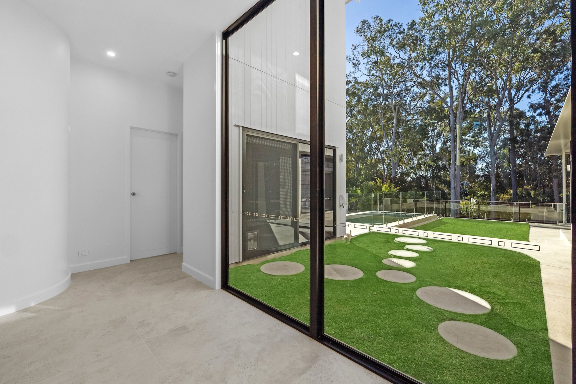 Interior view of a modern home with large glass sliding doors leading to a backyard with a lawn, stepping stones, and trees.