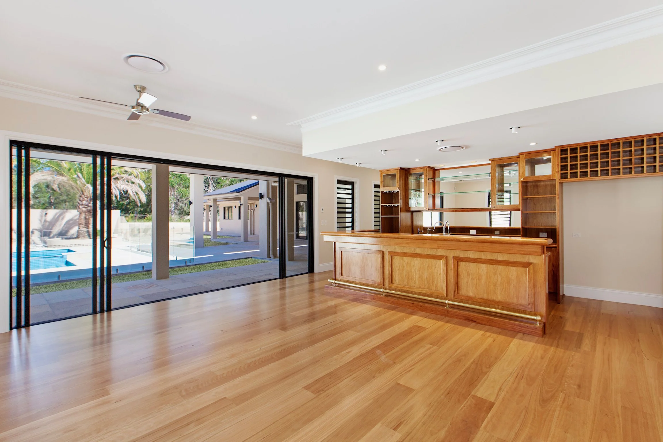 Interior of a house with sliding glass doors leading to a backyard pool, a wooden bar area, hardwood floors, ceiling fan, and recessed lighting.