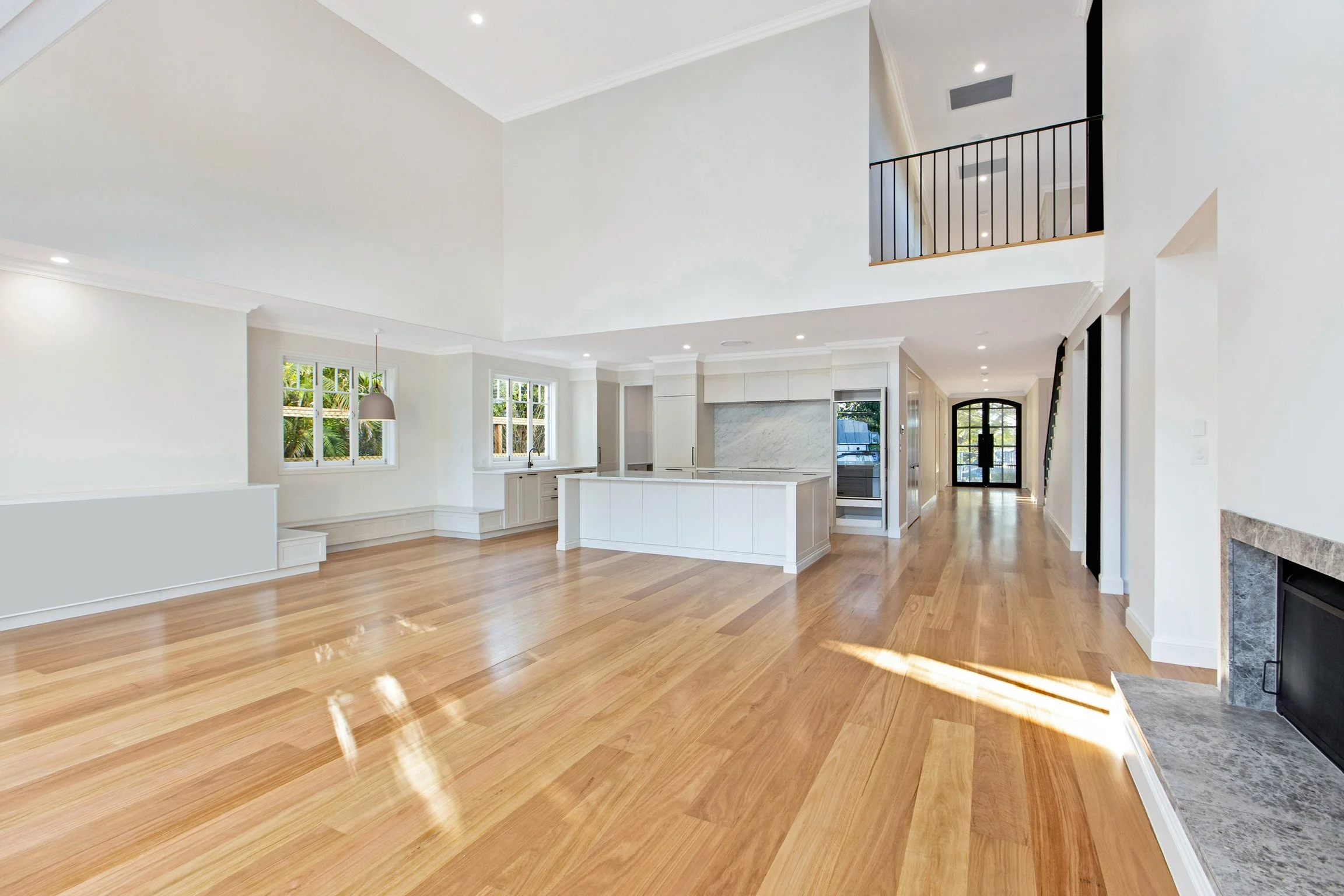 Spacious open-concept living area with hardwood floors, white walls, large windows, a modern kitchen with marble island, and a staircase leading to an upper floor.