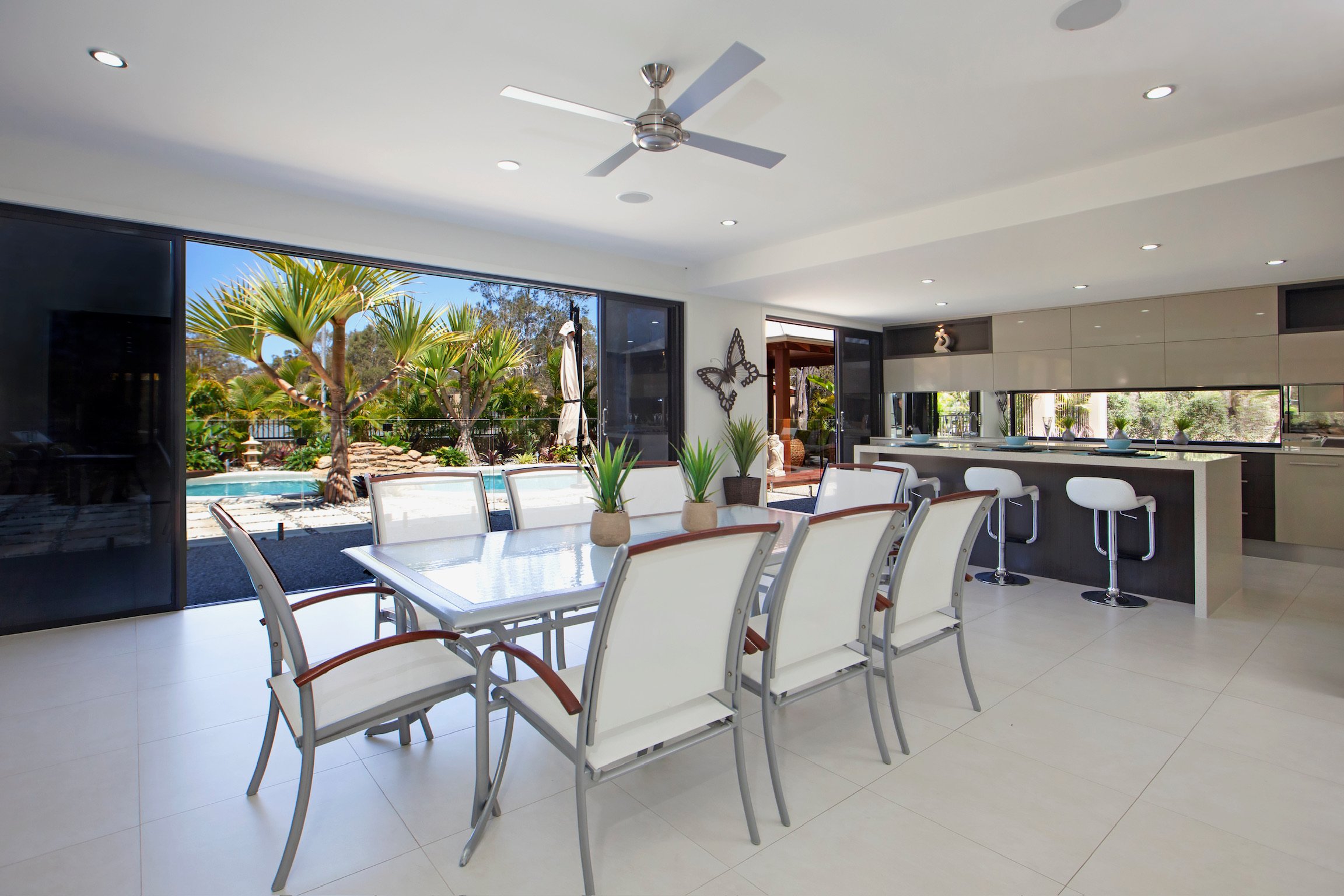 Modern indoor dining area with a view of a backyard featuring a swimming pool, palm trees, and outdoor seating.