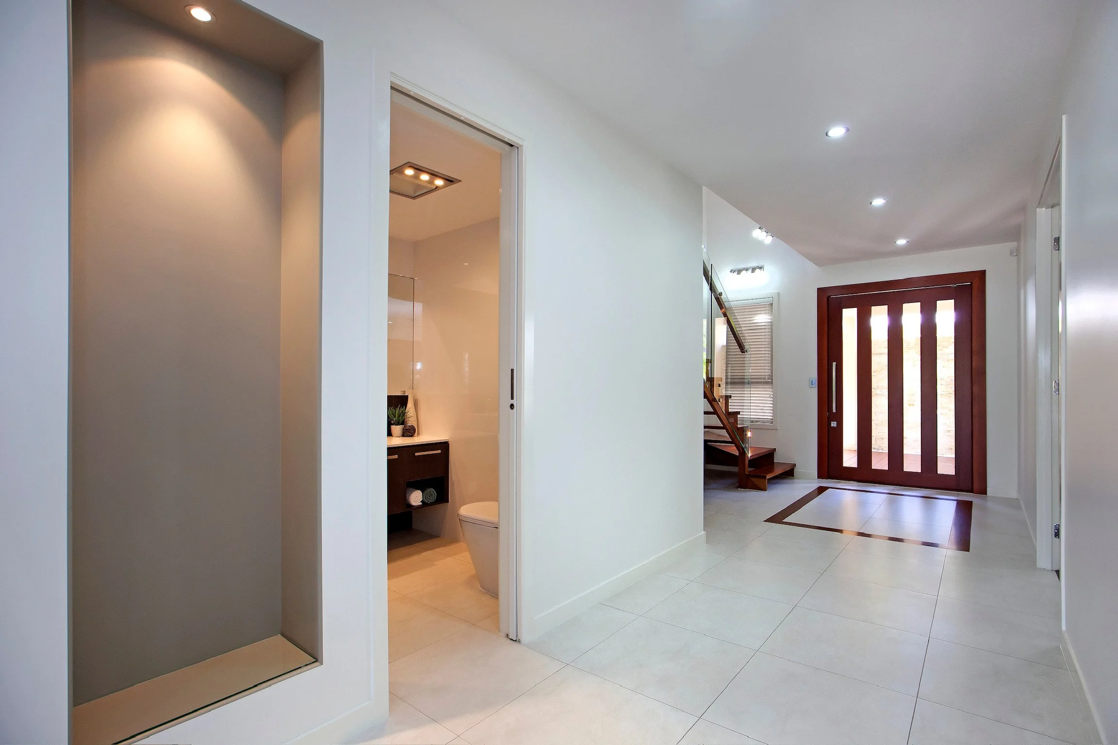 Modern entryway with front door, staircase, and a small bathroom with a toilet visible through an open door.