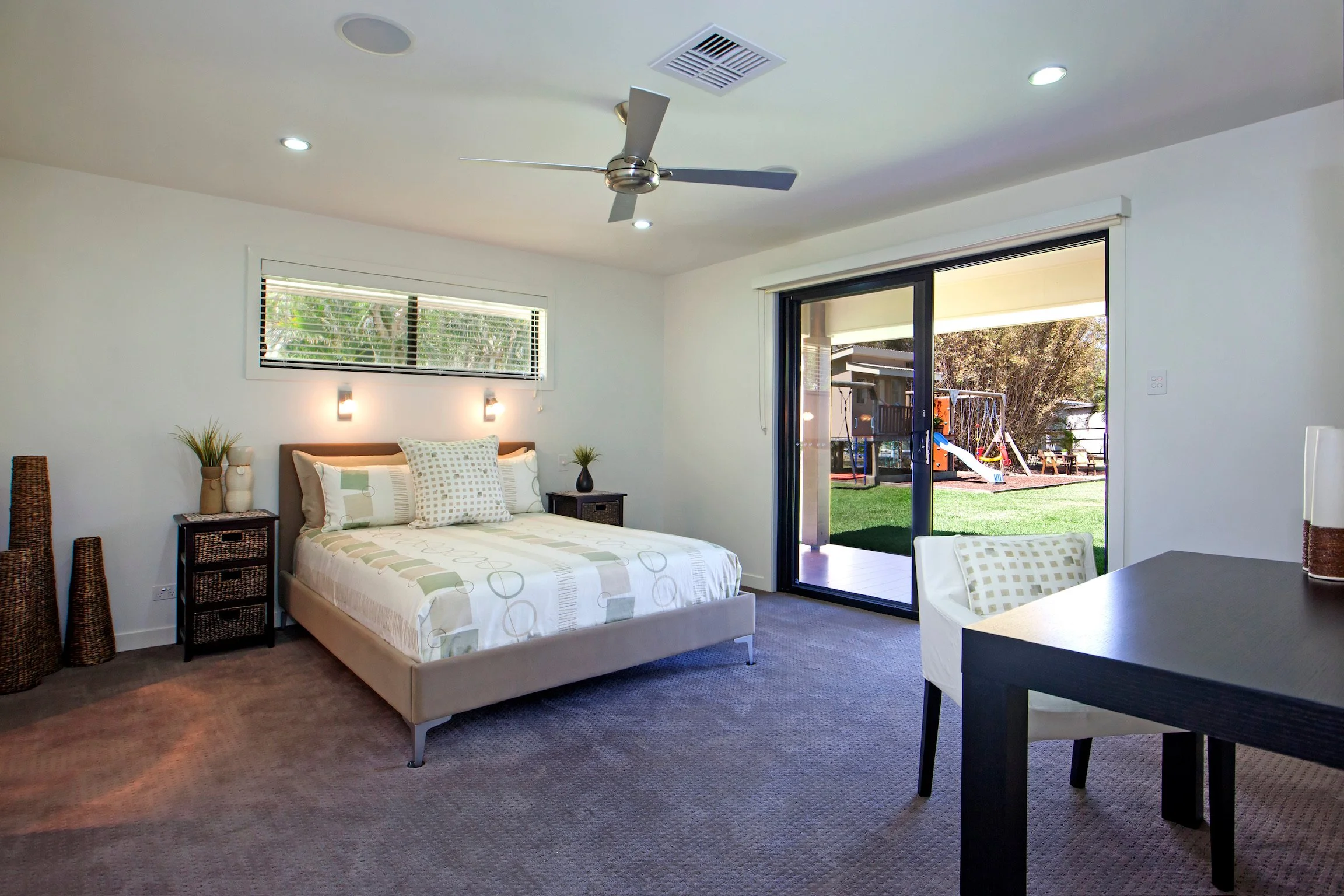 A bedroom with a bed, nightstands, and a sliding glass door leading to a backyard with a playground.