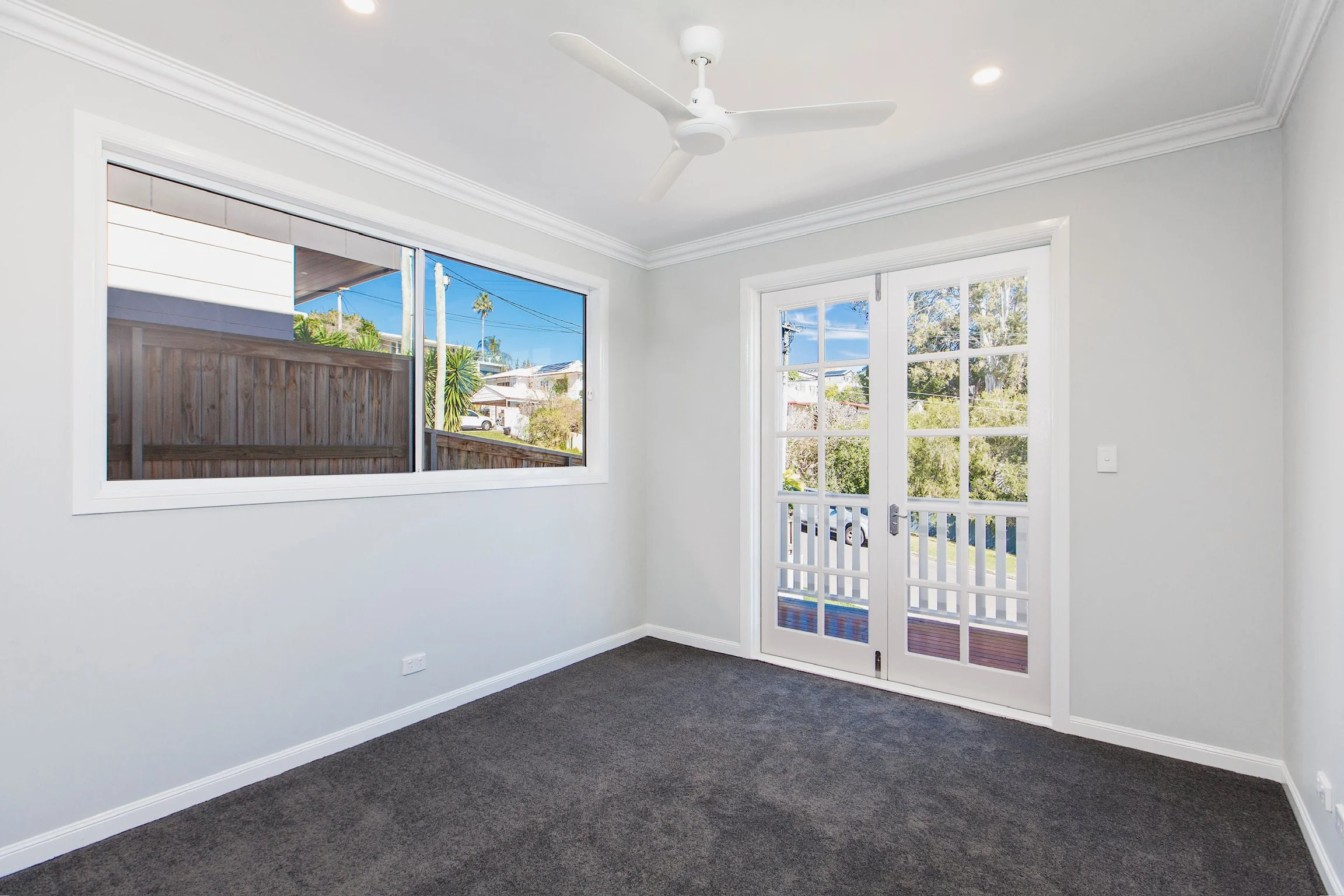 Empty room with gray carpet, white walls, large windows, and a white ceiling fan.