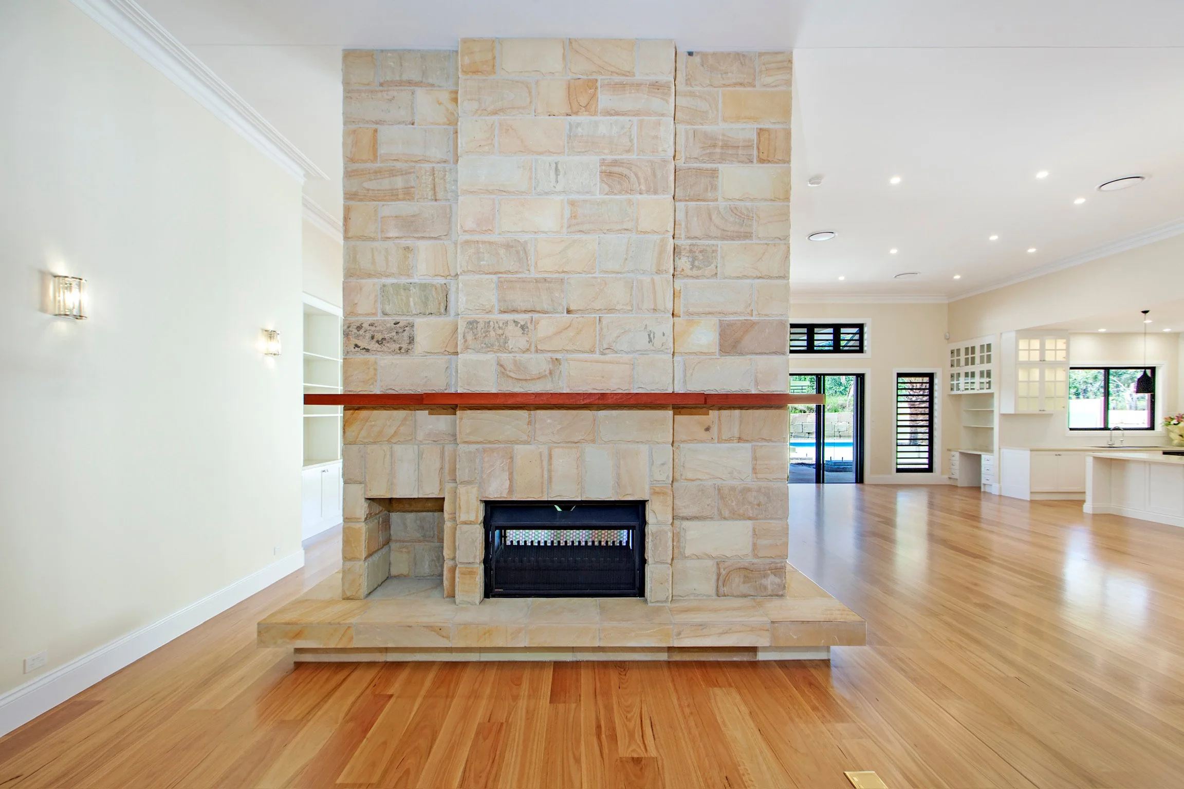Interior of a modern home with a stone fireplace at center, open floor plan, wooden floors, and large windows in the background.