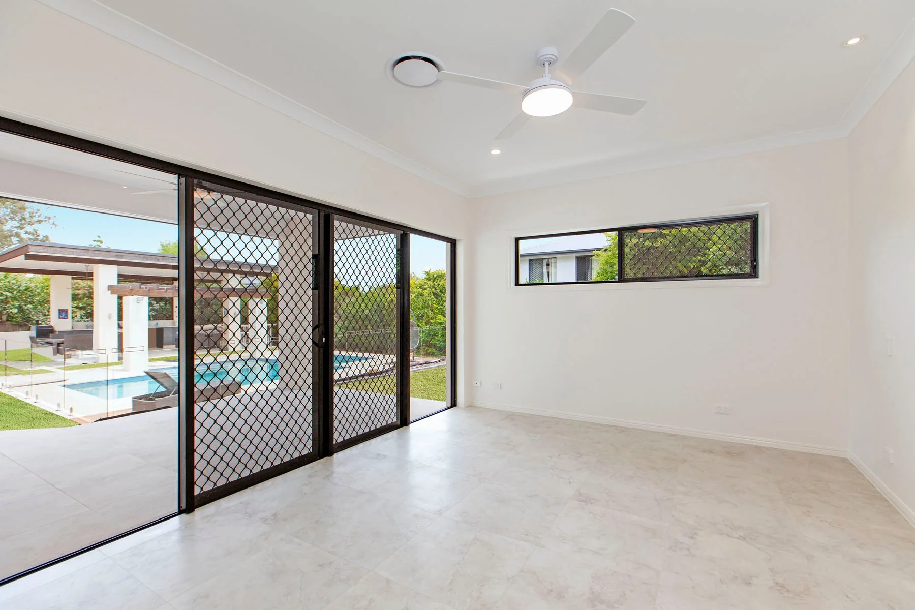 Empty room with large sliding glass doors and window showing a backyard with a swimming pool, outdoor seating, and greenery.