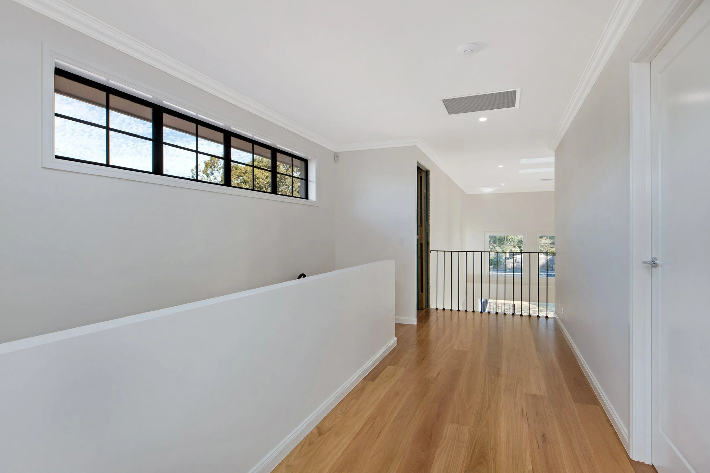 Interior of a modern, bright house with white walls, large horizontal windows, hardwood floors, and a staircase with a metal railing.