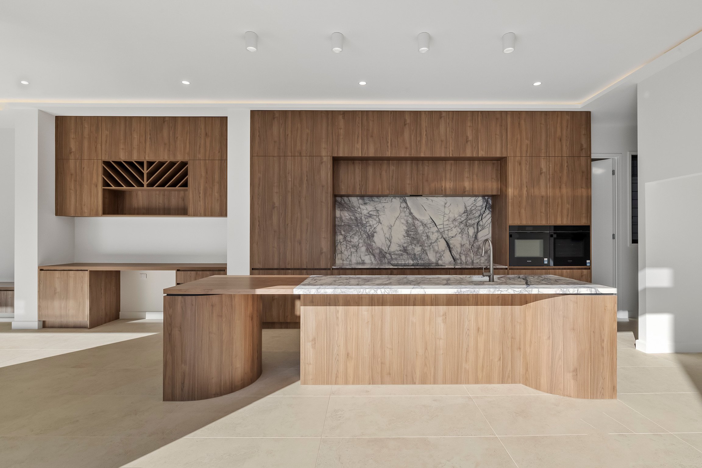 Modern kitchen with wooden cabinets, marble backsplash, and an island with a marble top.