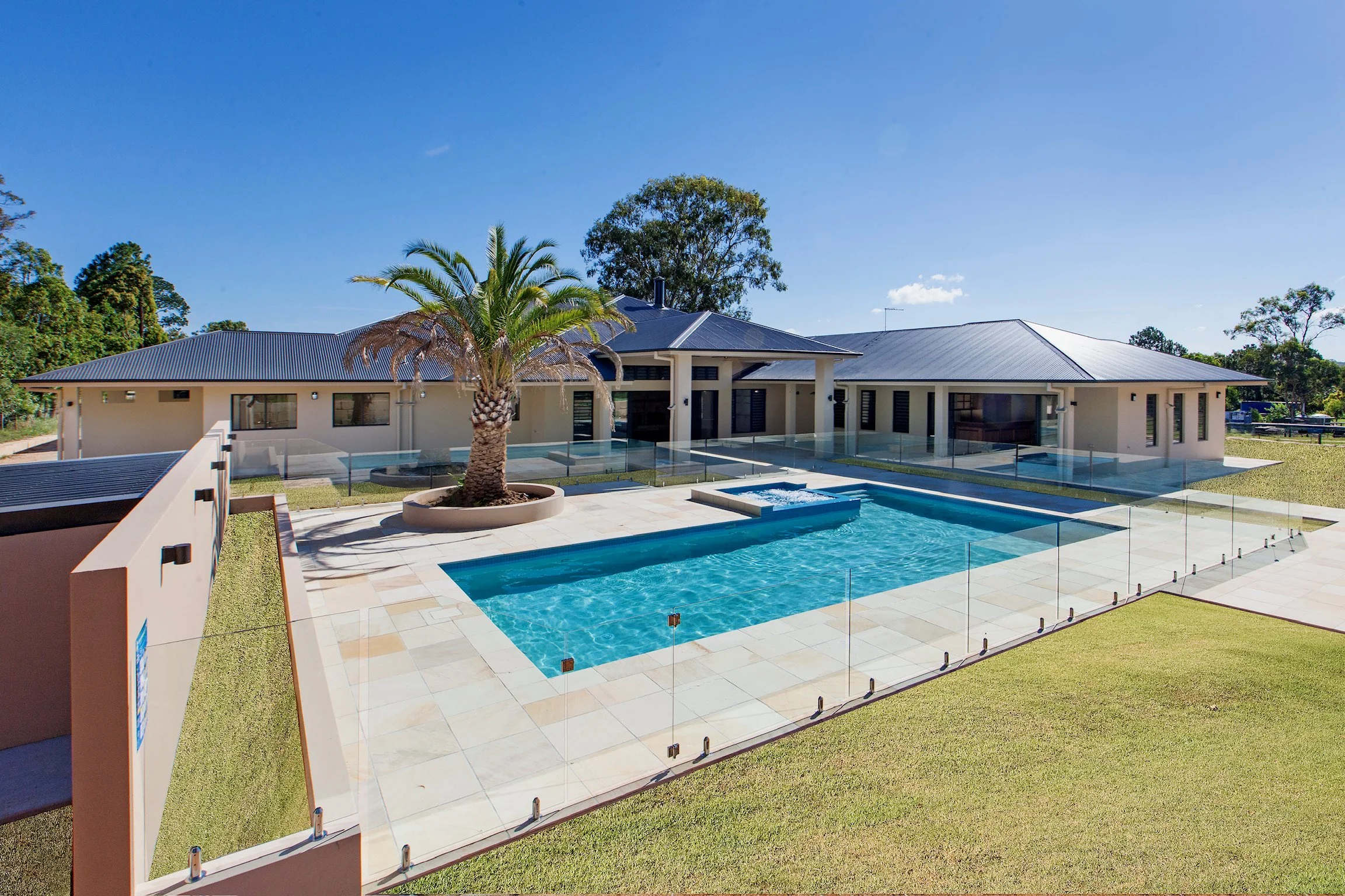 Modern house with a swimming pool, palm tree, and clear blue sky.
