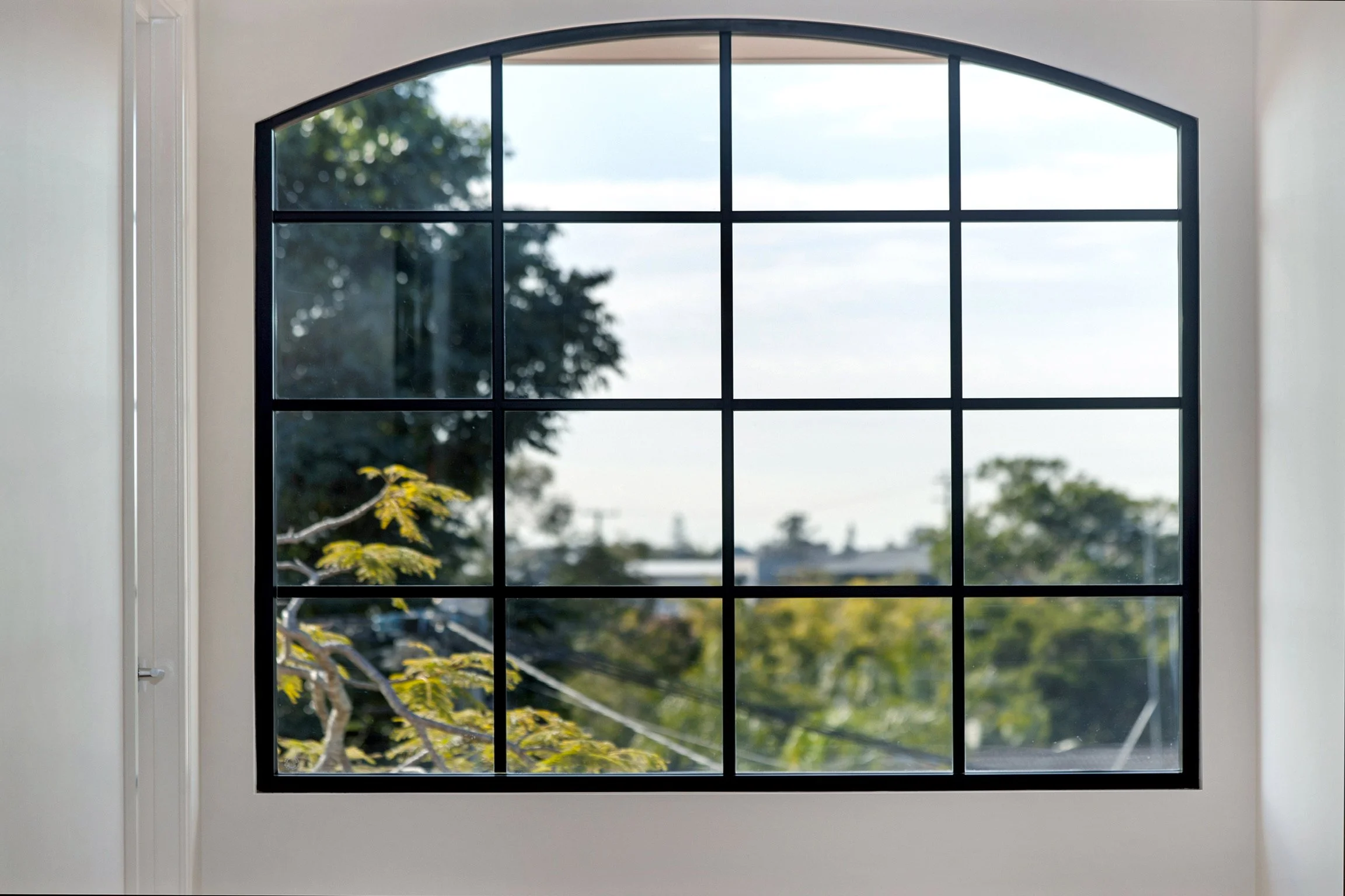 A large window with multiple panes, looking out onto trees and a cloudy sky while sunlight filters through.