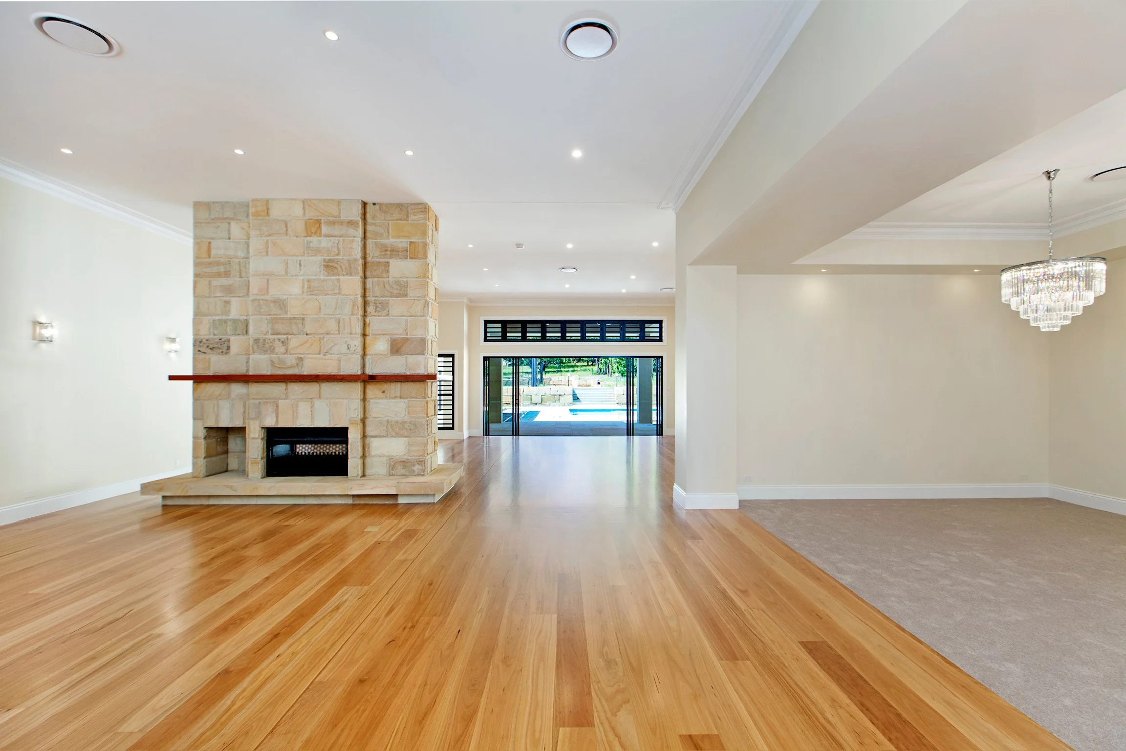 Interior of a spacious living room with hardwood floors, a stone fireplace, large windows, and a modern chandelier.
