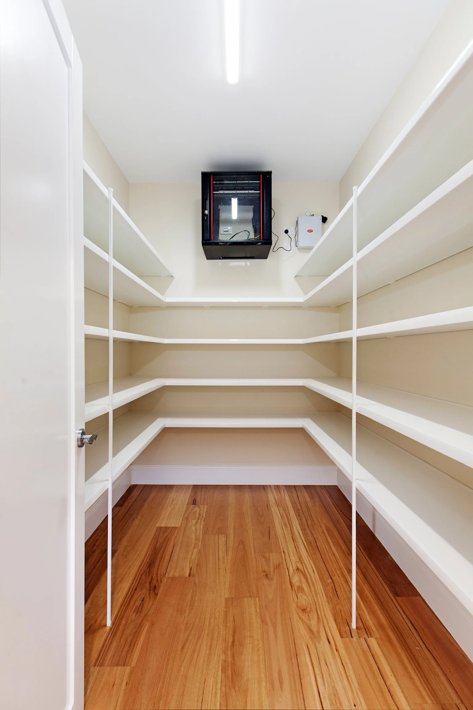 Empty walk-in closet with white built-in shelves, hardwood floors, and a ceiling mounted light fixture.