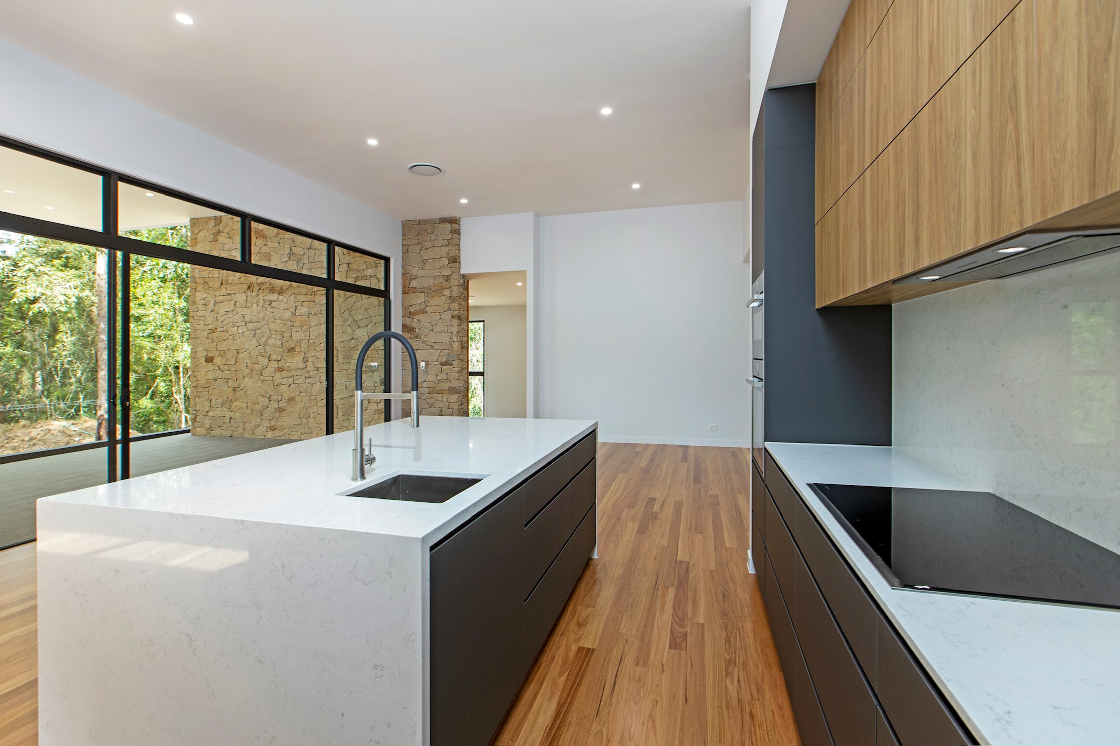 Modern kitchen with white island, black cabinets, and wooden flooring, large windows, and stone wall accents.