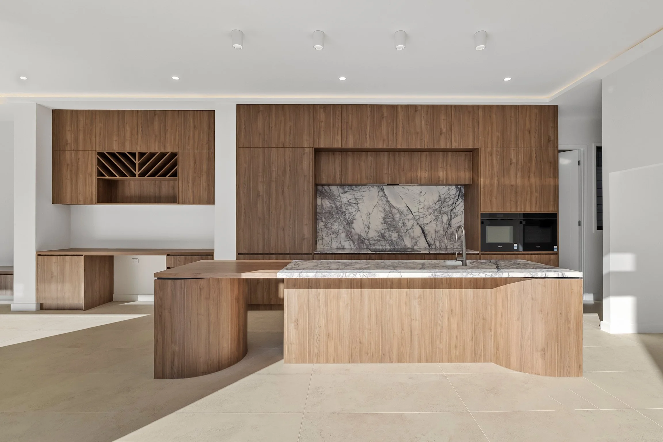 Modern kitchen with wooden cabinetry, marble island, and built-in appliances.