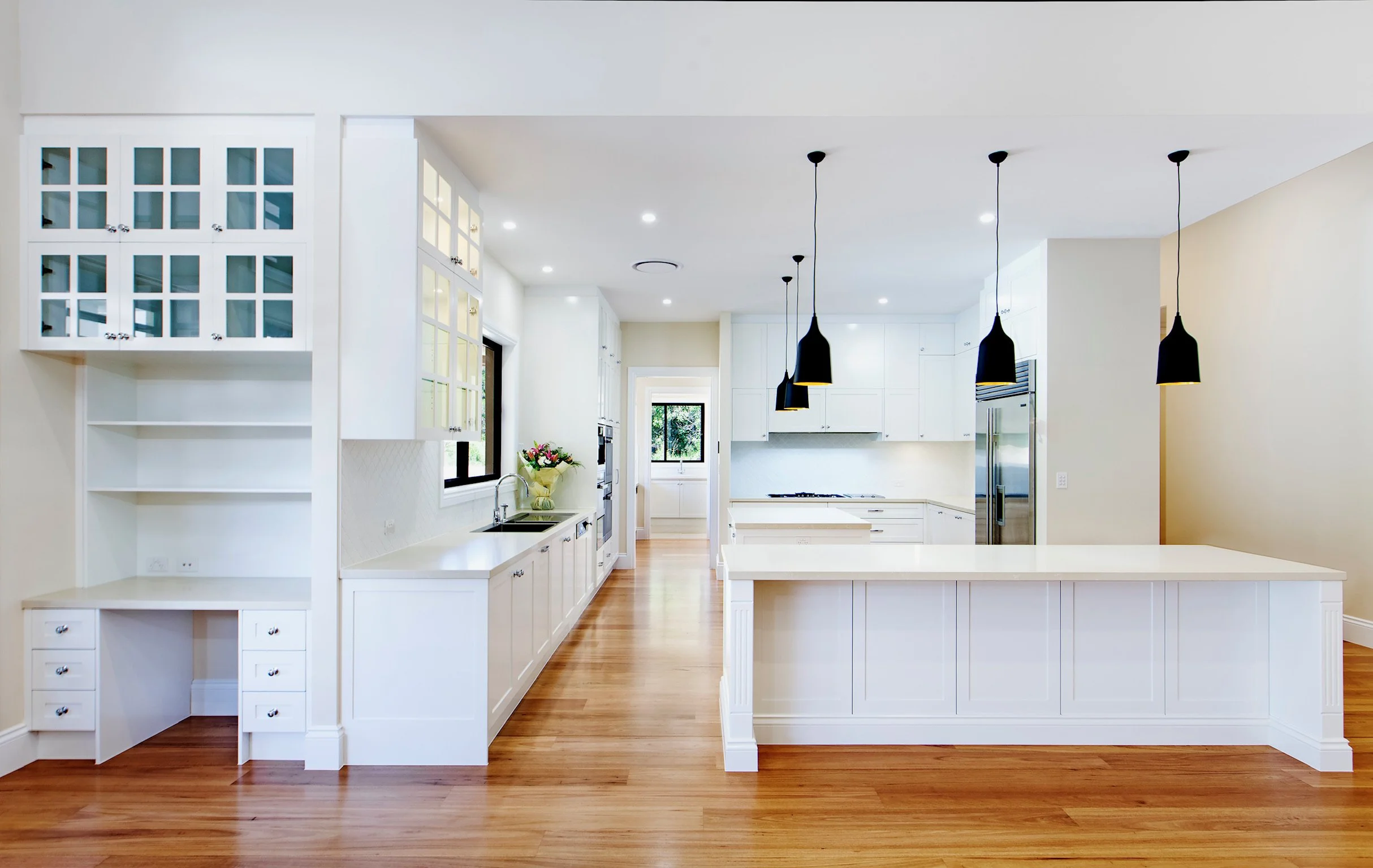 Bright white farmhouse-style kitchen with white cabinets, black pendant lights, and hardwood floors.
