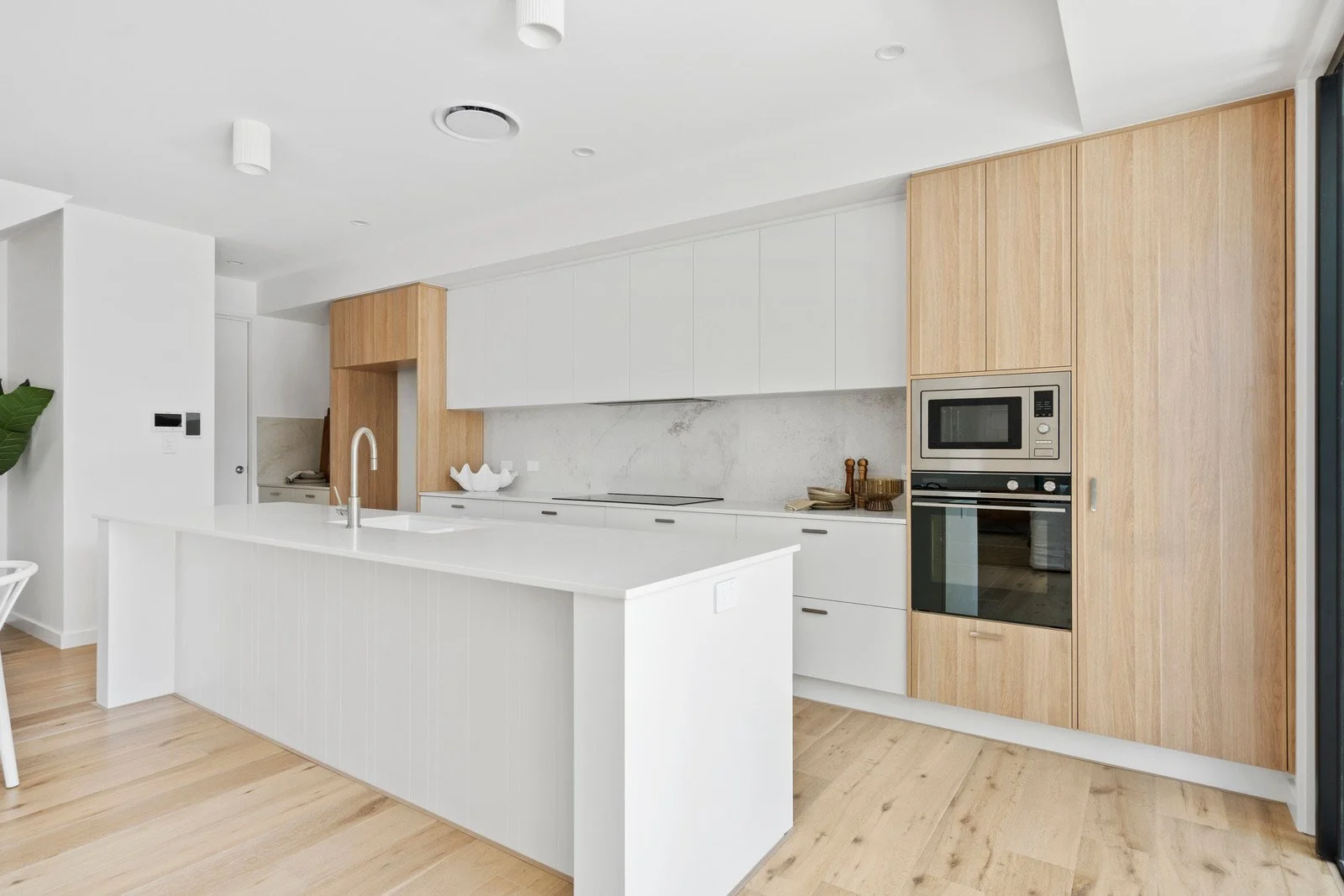 Modern minimalist kitchen with white cabinetry, wooden accents, and built-in appliances. Features a large island with a sink and faucet, and wooden flooring.