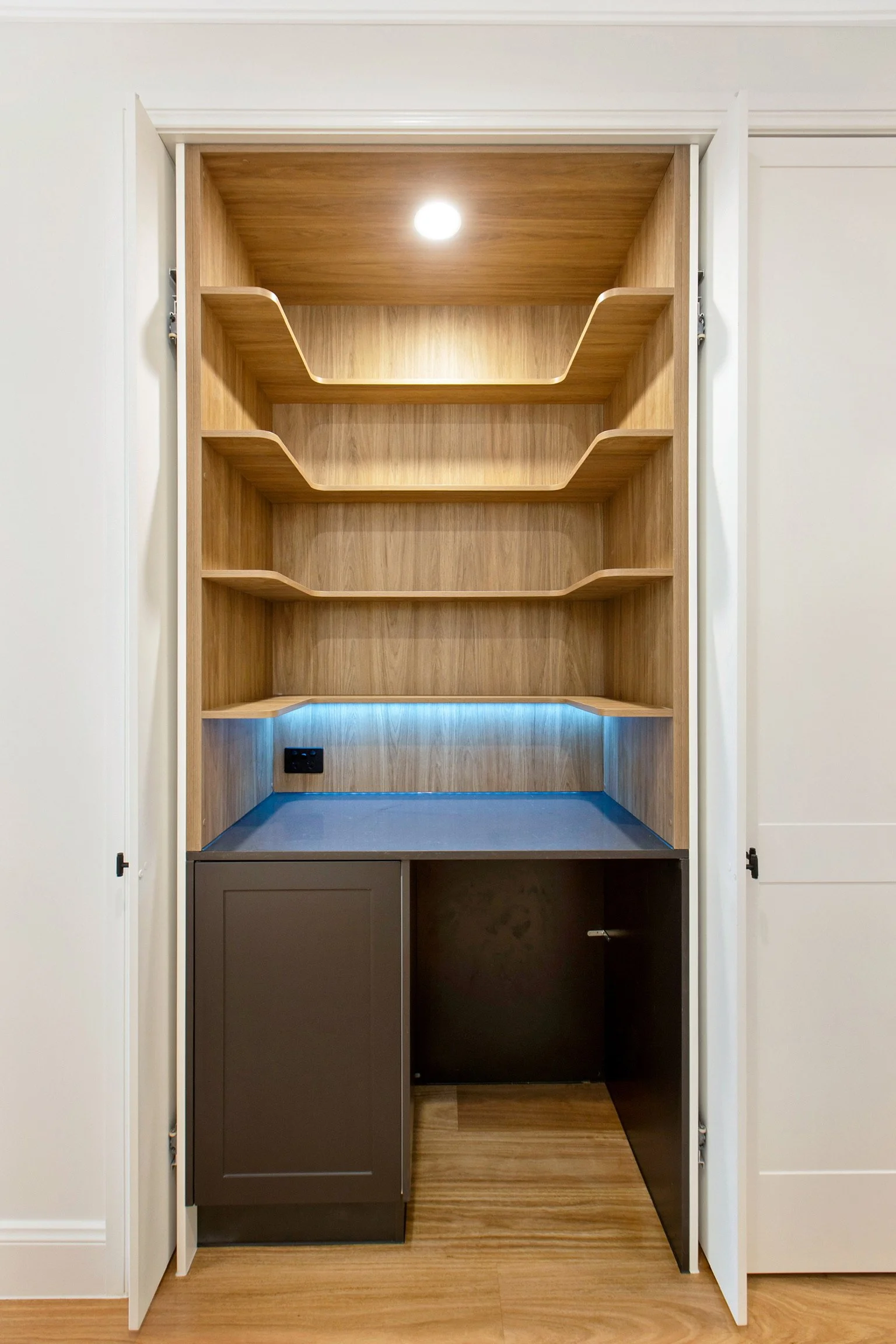 Open kitchen cabinet with wooden shelves, black lower cabinet, and electrical outlet inside.
