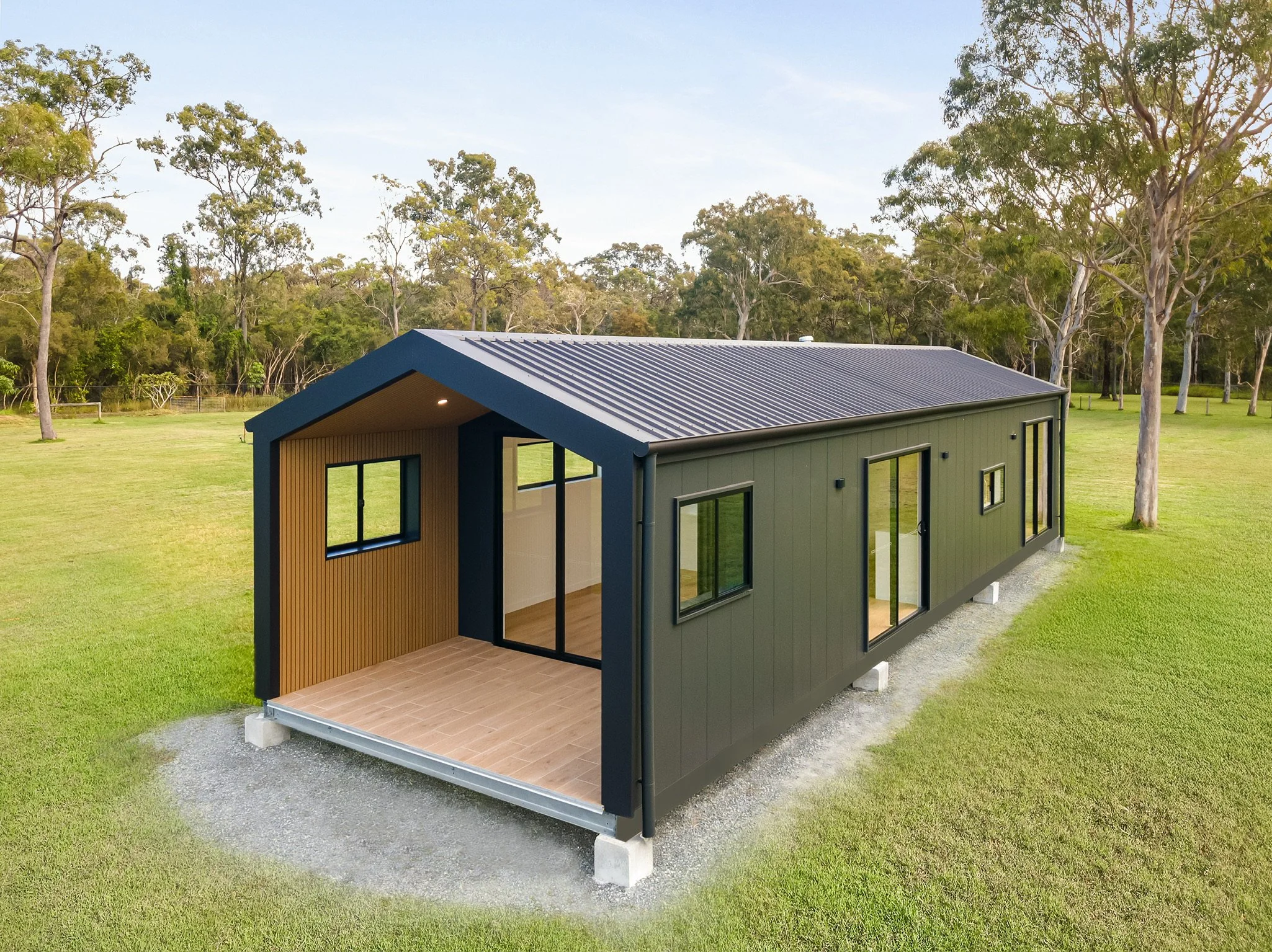 Modern tiny house with black exterior, gabled roof, large windows, and a covered porch, situated on a grassy field with trees in the background.