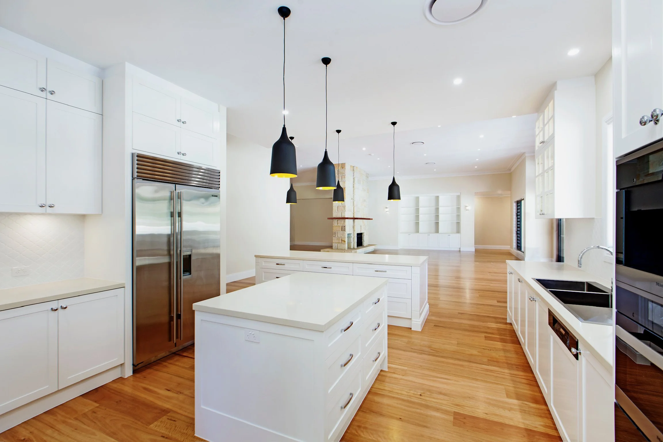 Modern kitchen with white cabinets, stainless steel refrigerator, black pendant lights, and hardwood floors.