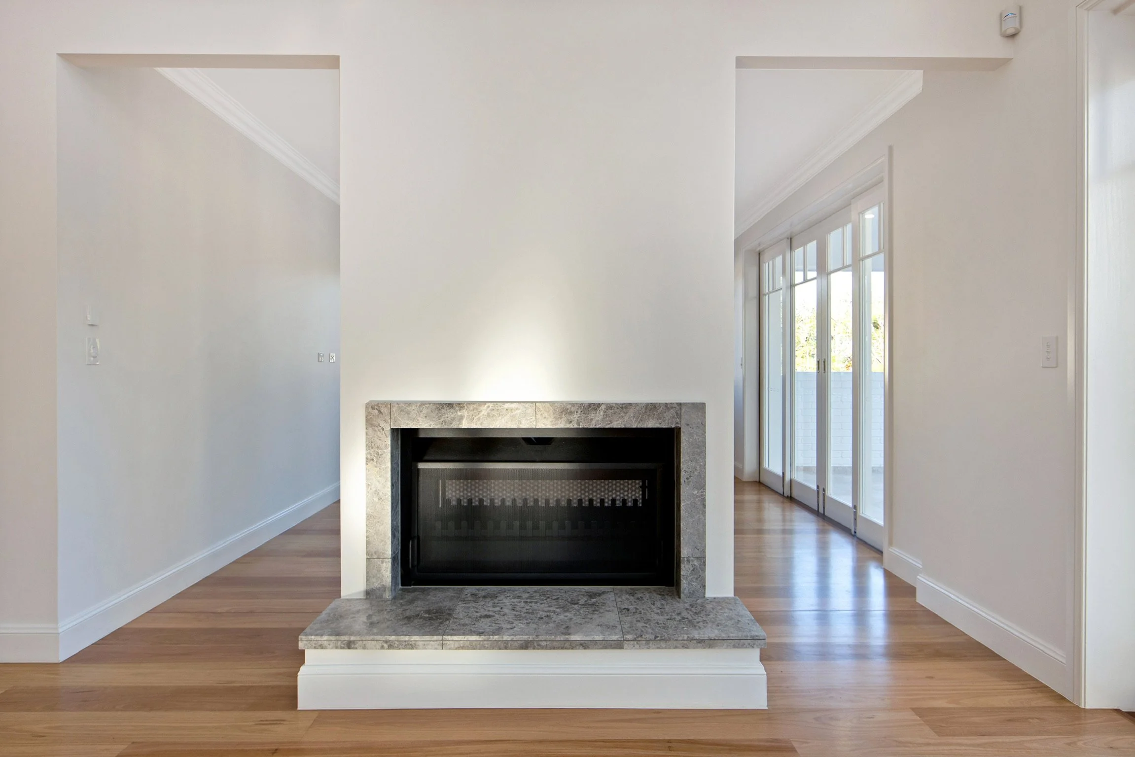 Living room with a white wall, marble fireplace, hardwood floors, and large glass sliding doors leading to an outdoor balcony.