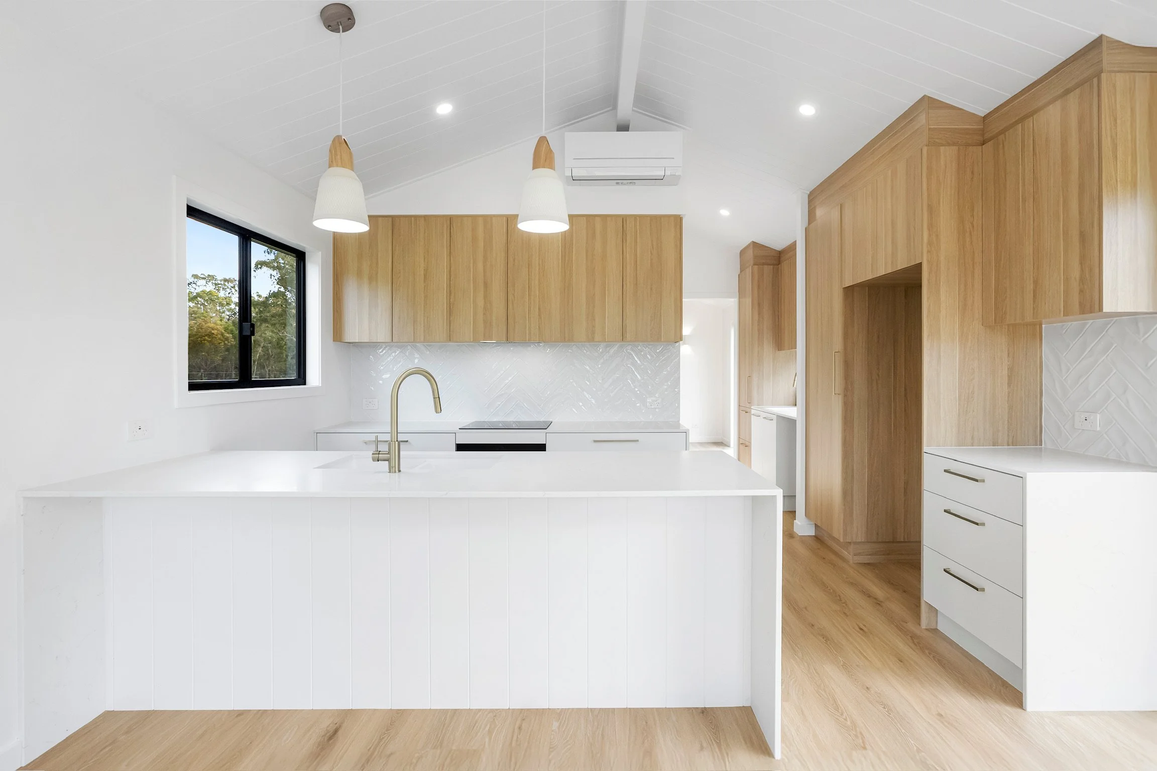 Modern kitchen with white countertops, wooden cabinetry, and large window with outside view.