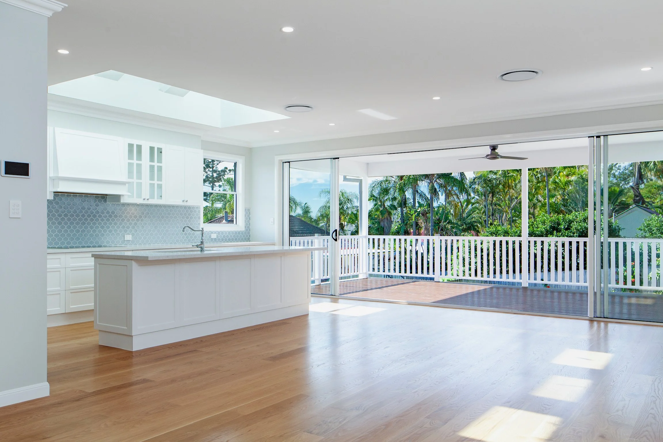 Bright, open kitchen and living area with sliding glass doors leading to a balcony with trees outside.