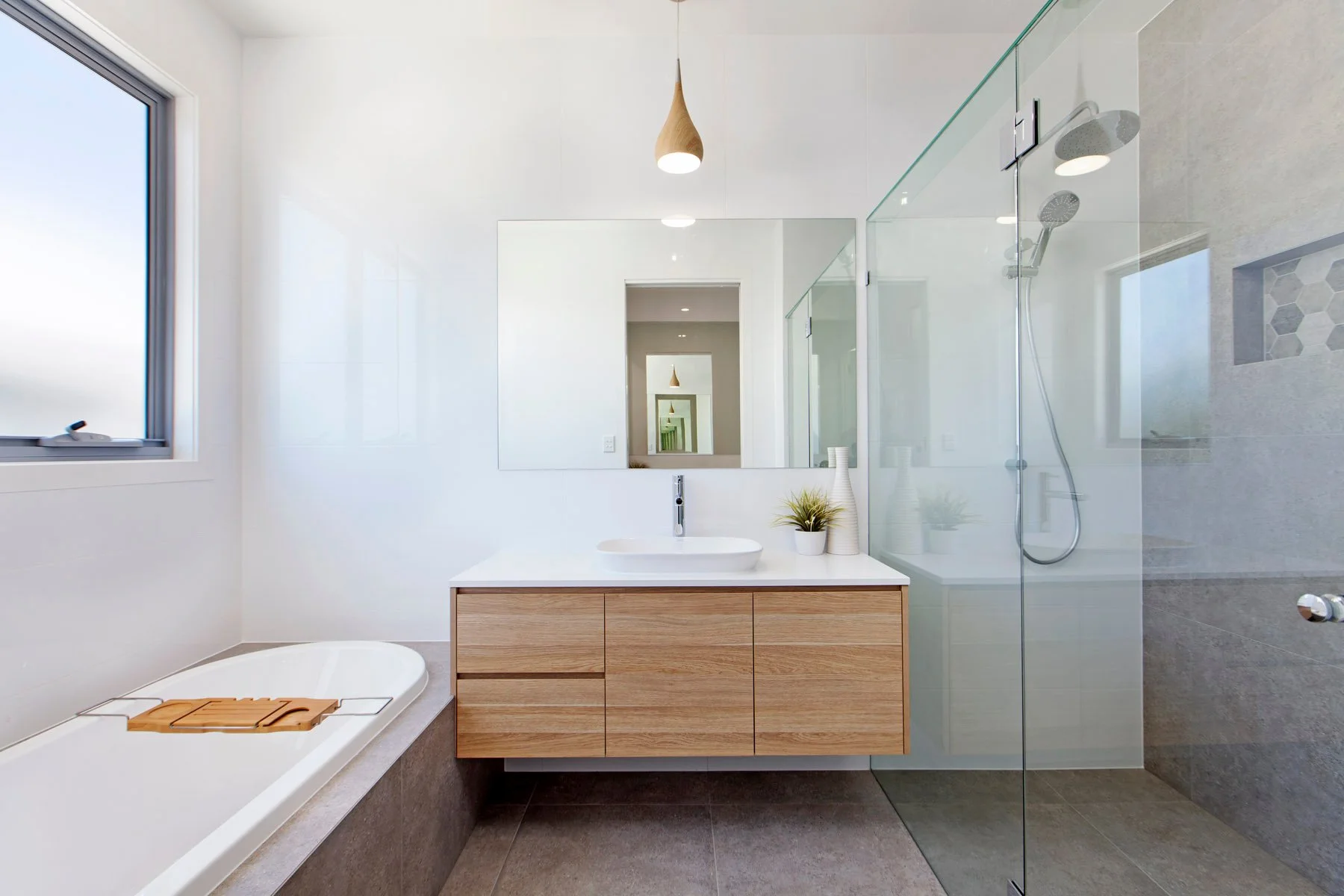 Modern bathroom with a walk-in shower, vanity with a vessel sink, mirror, and small decorative plants, natural light coming from a window, neutral color scheme.
