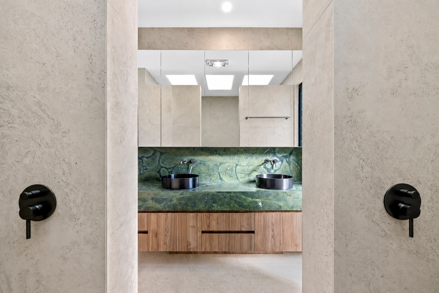 Modern bathroom with double sinks, black countertops, green marble backsplash, wooden vanity, and mirrored cabinets.