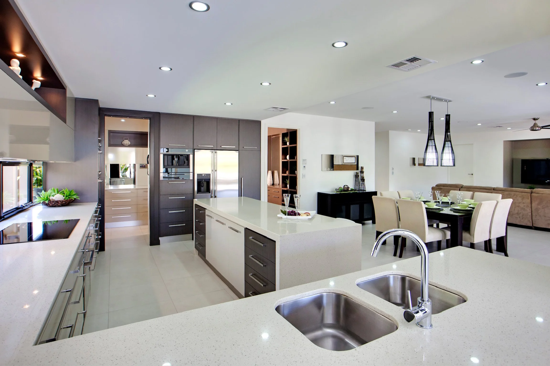 Modern kitchen with white countertops, gray cabinets, and a dining area with cream chairs, a black sideboard, and pendant lighting.