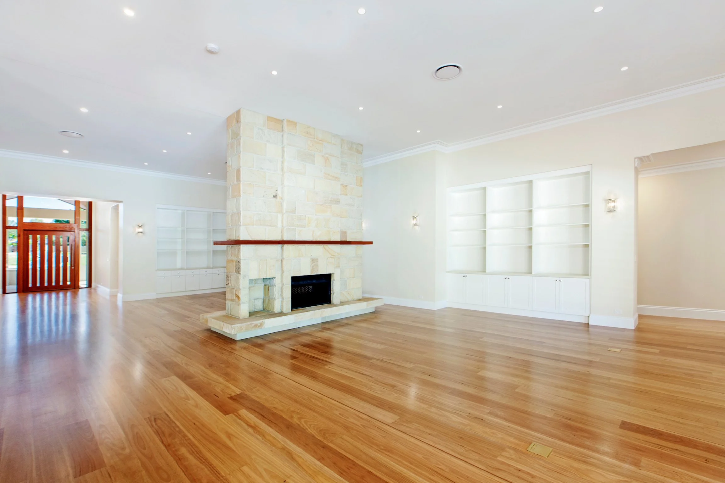 Empty living room with hardwood floors, a stone fireplace, white built-in shelves, and a door leading outside.