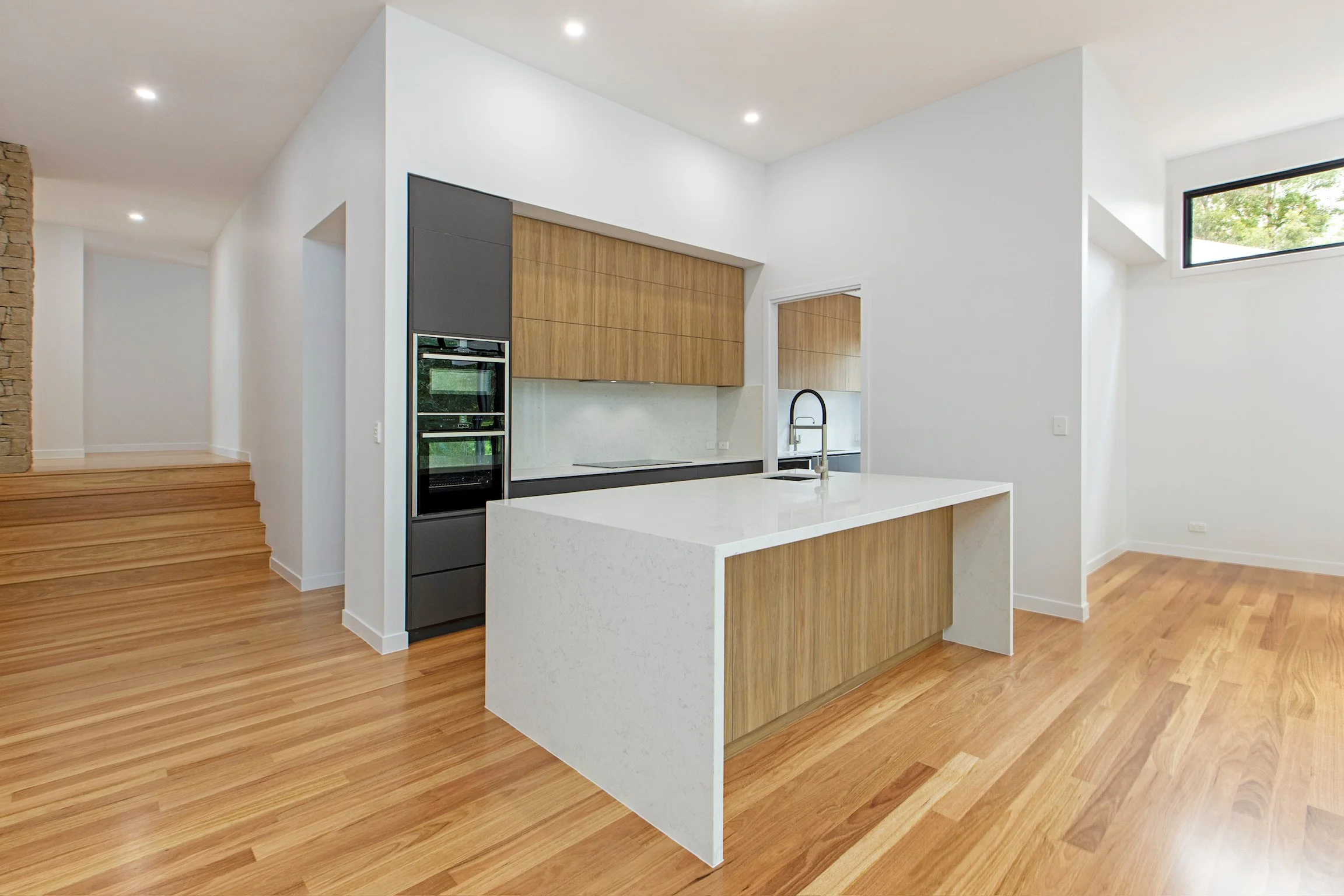 Modern kitchen with wooden cabinets, white countertops, and hardwood floors, featuring a kitchen island and outlet.