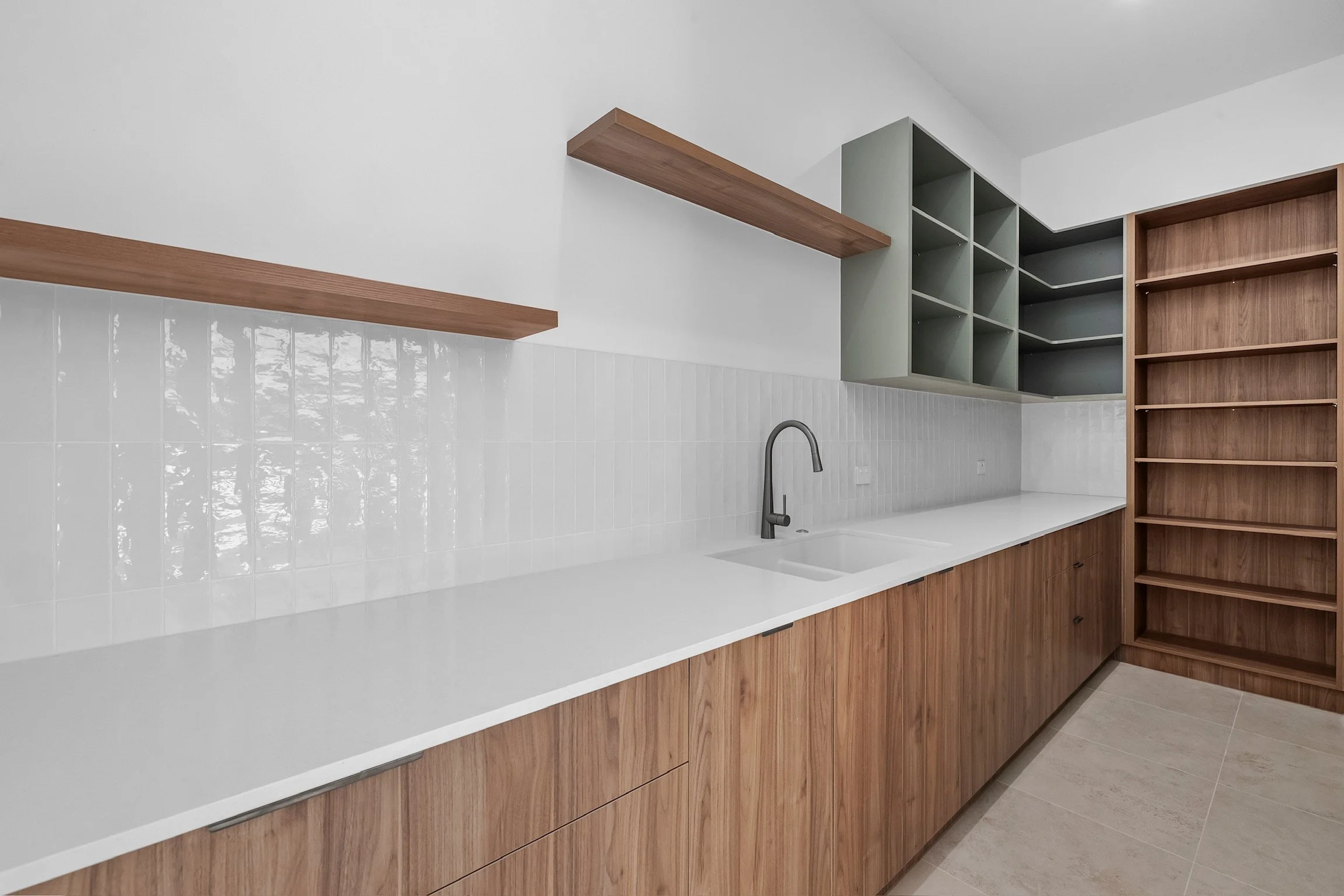 Modern kitchen with white countertop, wooden cabinets, open shelving, and a black faucet in the sink area.