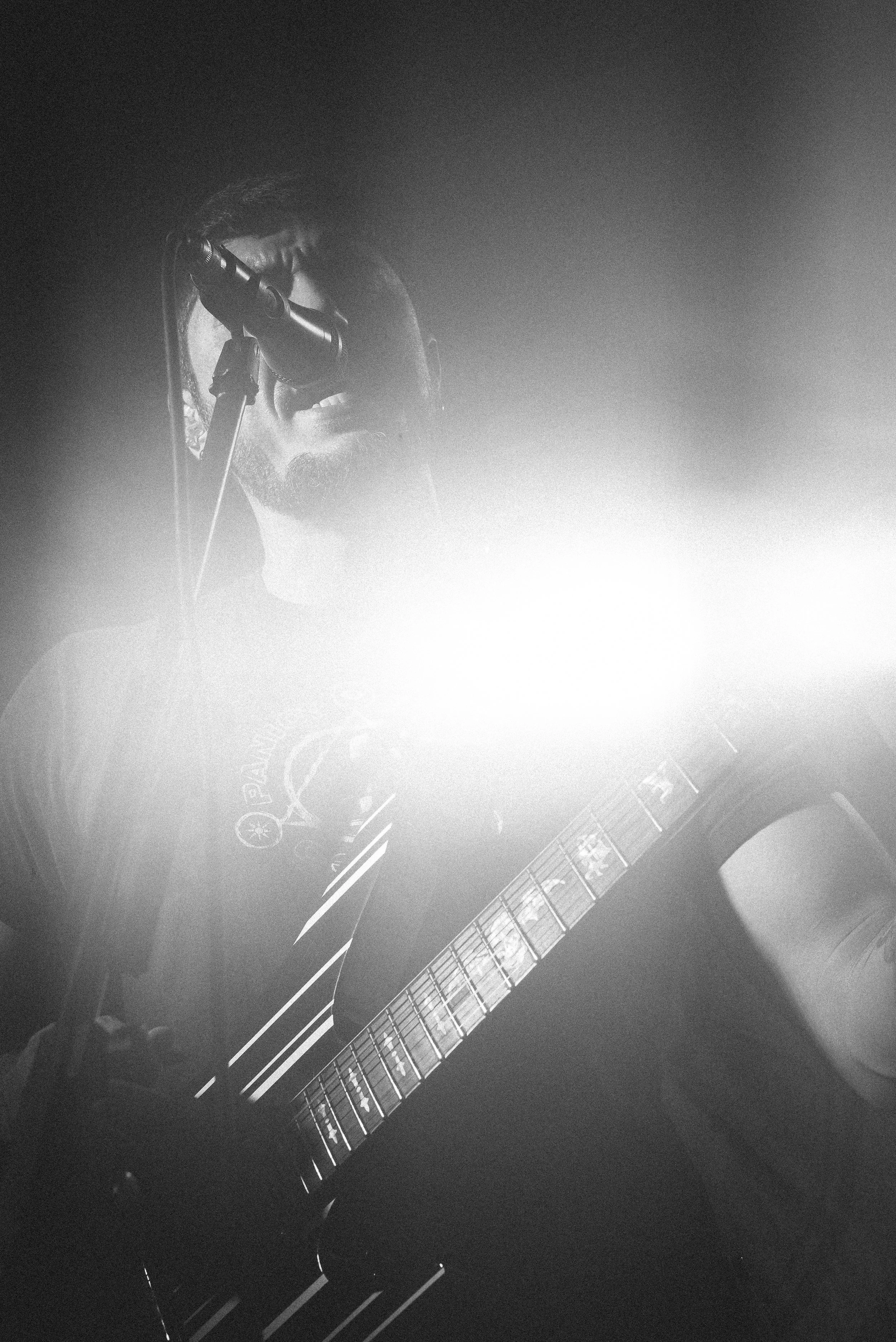 Black and white image of a man playing an acoustic guitar, wearing sunglasses, in a dimly lit setting.
