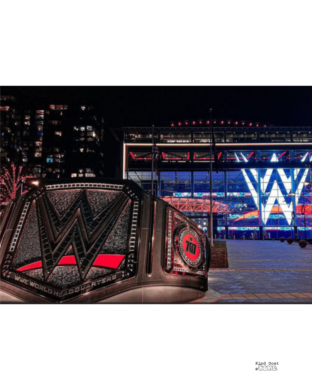 Nighttime view of a WWE World Headquaters sign with a large WWE logo in the background, illuminated in blue and white, outside a modern building.