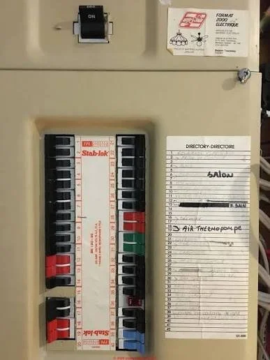 Close-up of an vintage beige Federal Pioneer Stab-Lok electrical panel showing red, black, green, and blue circuit breakers alongside a handwritten directory index.