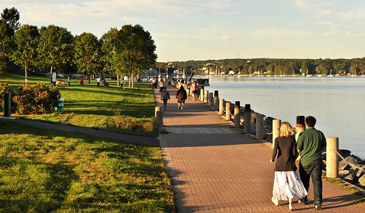 People walking along the waterfront boardwalk at DeWolf Park in Bedford, Nova Scotia, overlooking the Bedford Basin.
