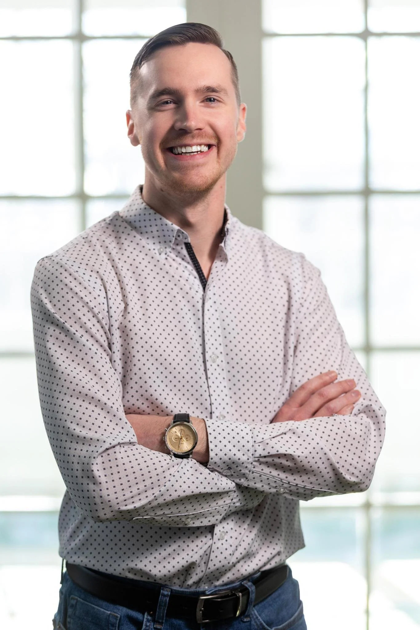 Professional portrait of Zach Surette smiling with arms crossed in a patterned button-down shirt.