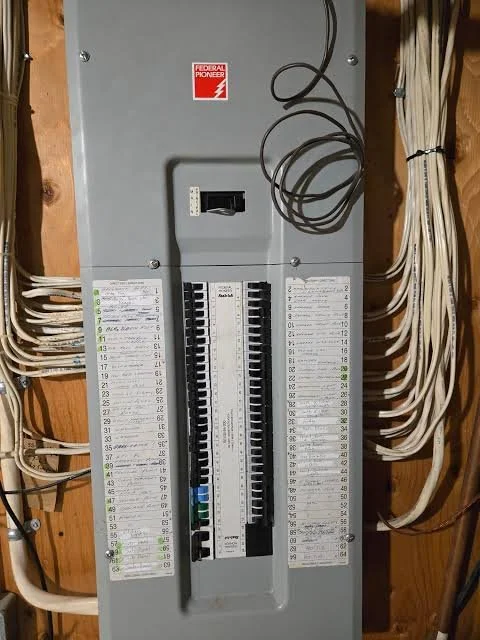 A vertical grey Federal Pioneer electrical panel mounted on a plywood wall with visible exposed wiring and circuit directories.