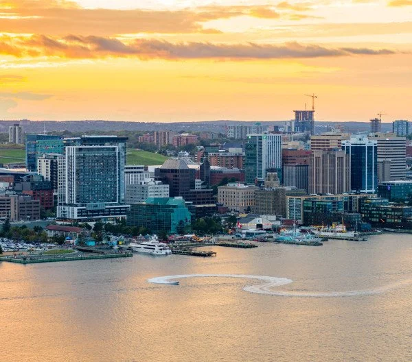 City skyline with modern buildings along a river at sunset.