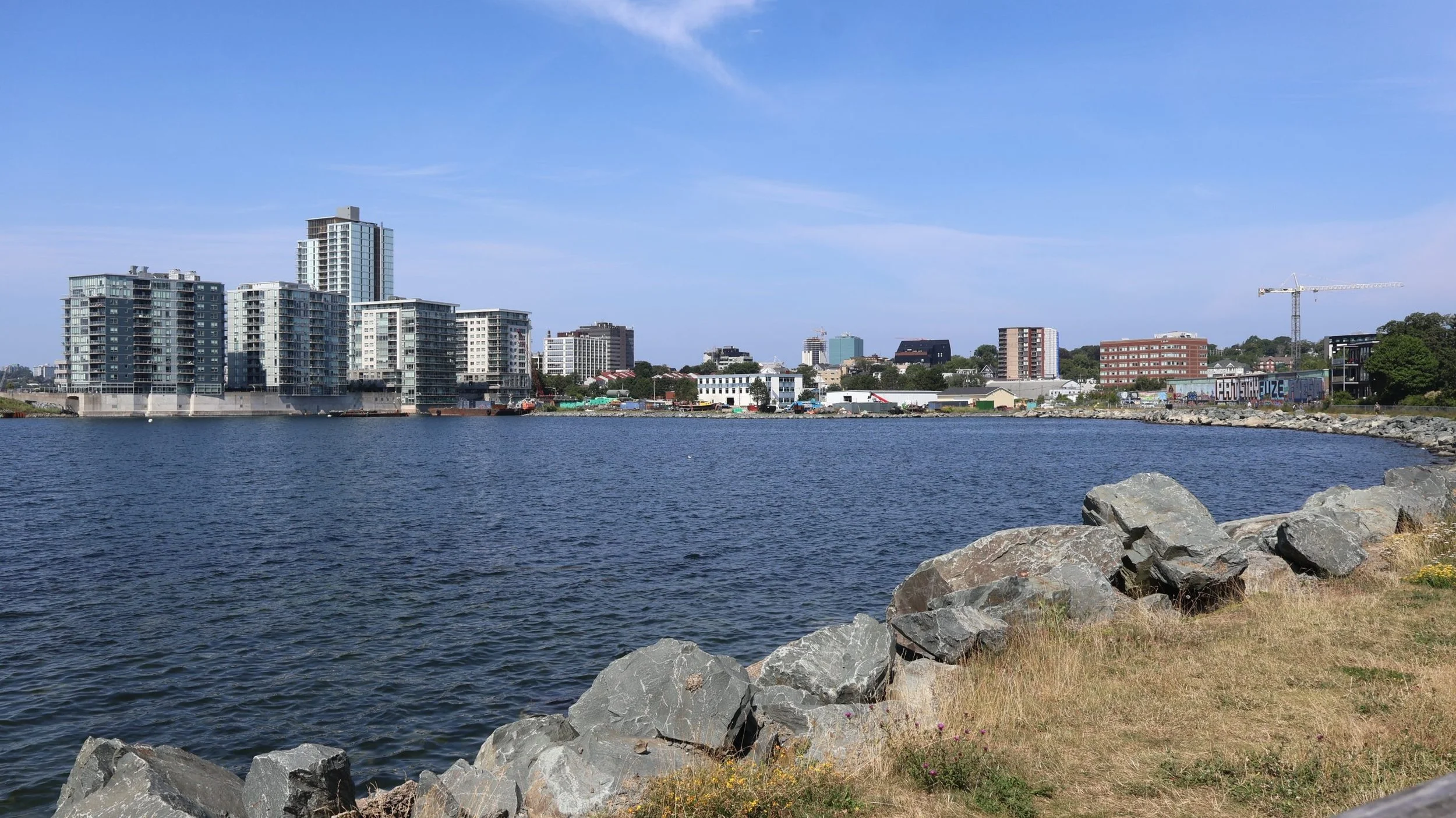 Rocky shoreline and walking trail along Dartmouth Cove looking toward modern waterfront residential condominiums in Dartmouth, Nova Scotia.