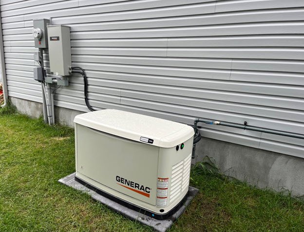 An outdoor Generac standby backup generator installed on a concrete pad against light grey vinyl siding next to an electrical transfer switch box.
